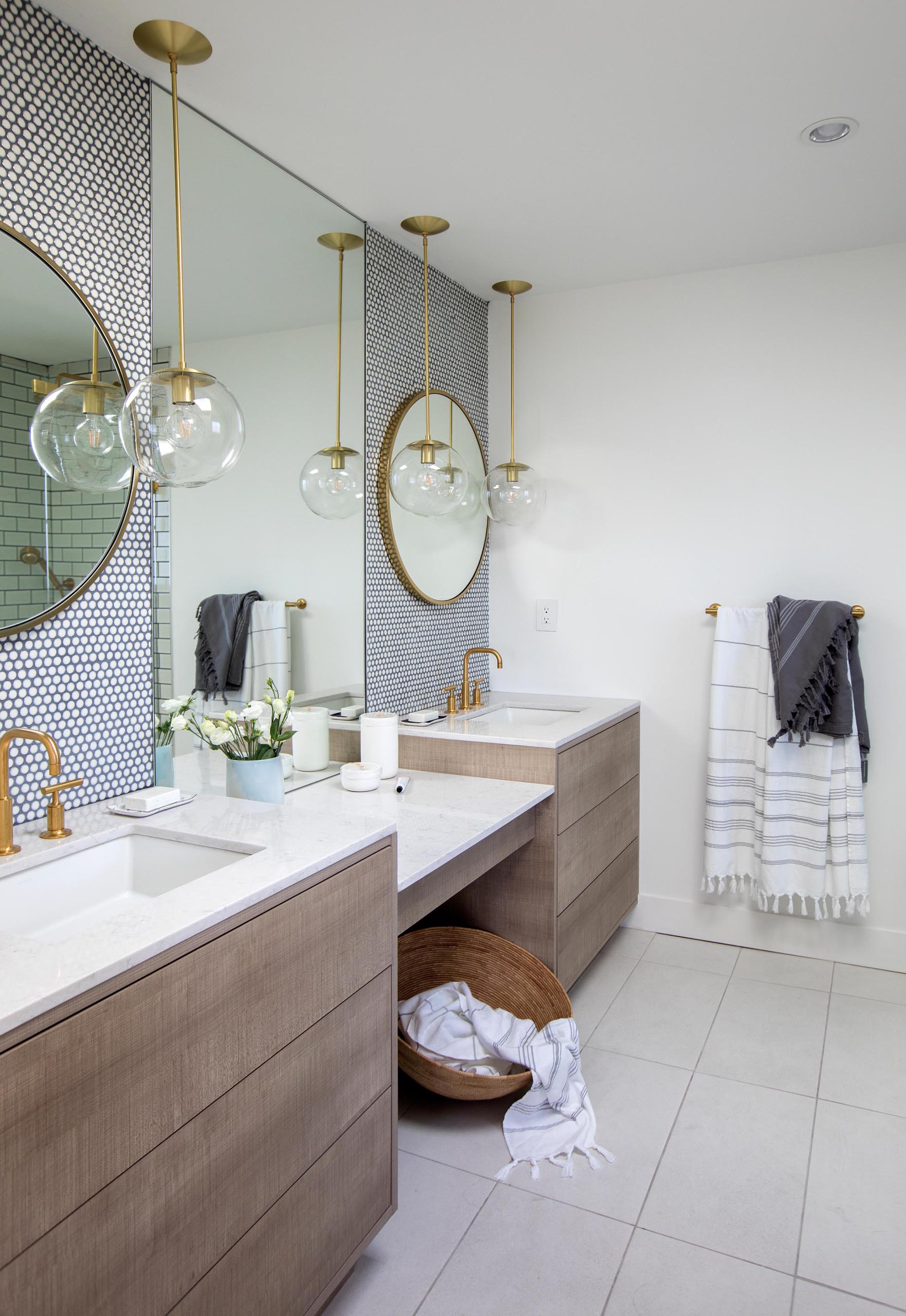 This modern master bathroom includes penny tile with dark grout, a wood vanity with a drop down countertop between the sinks.