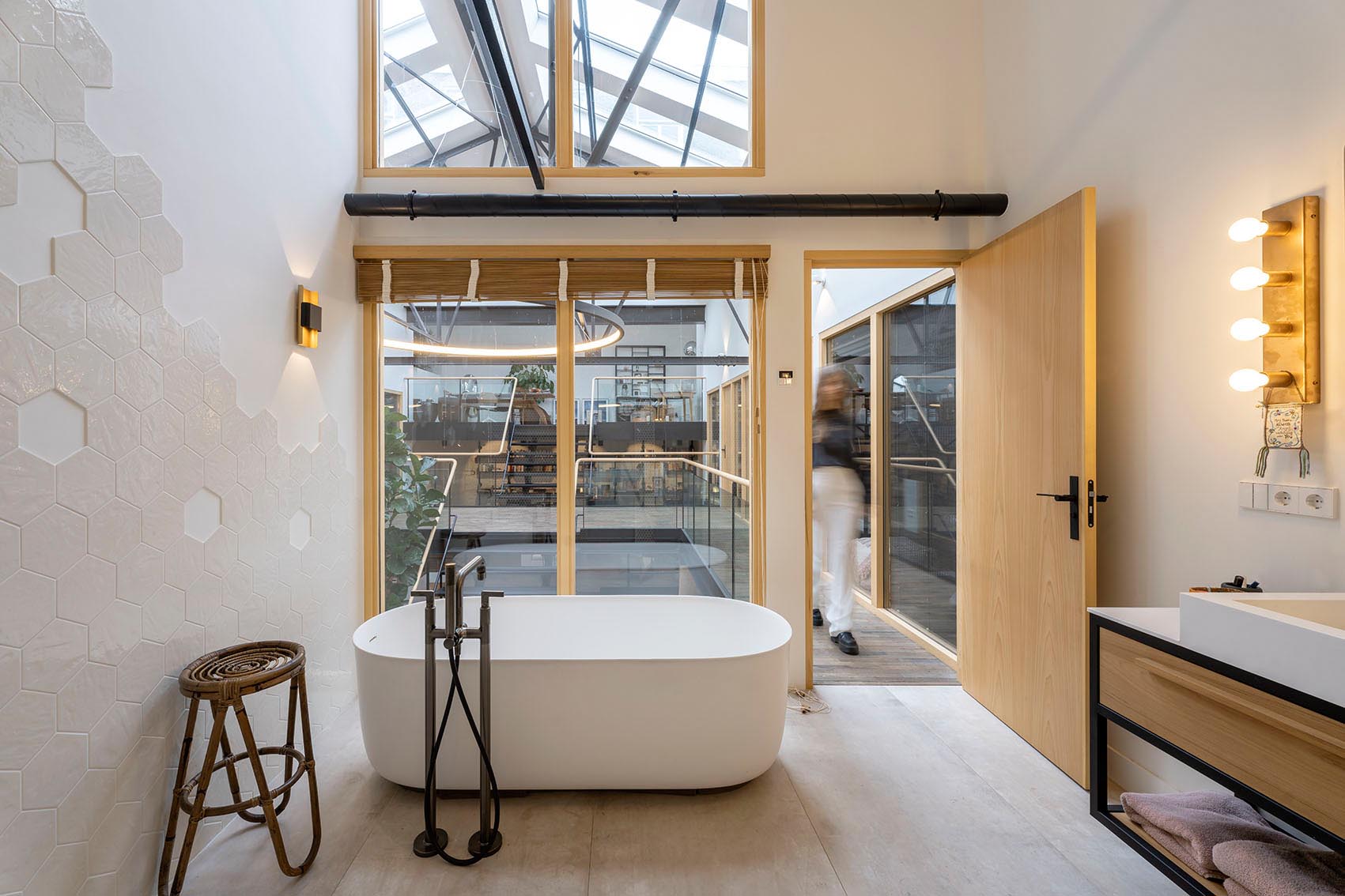 A modern bathroom with hexagonal tiles and a freestanding bathtub hat looks out to the floor below.