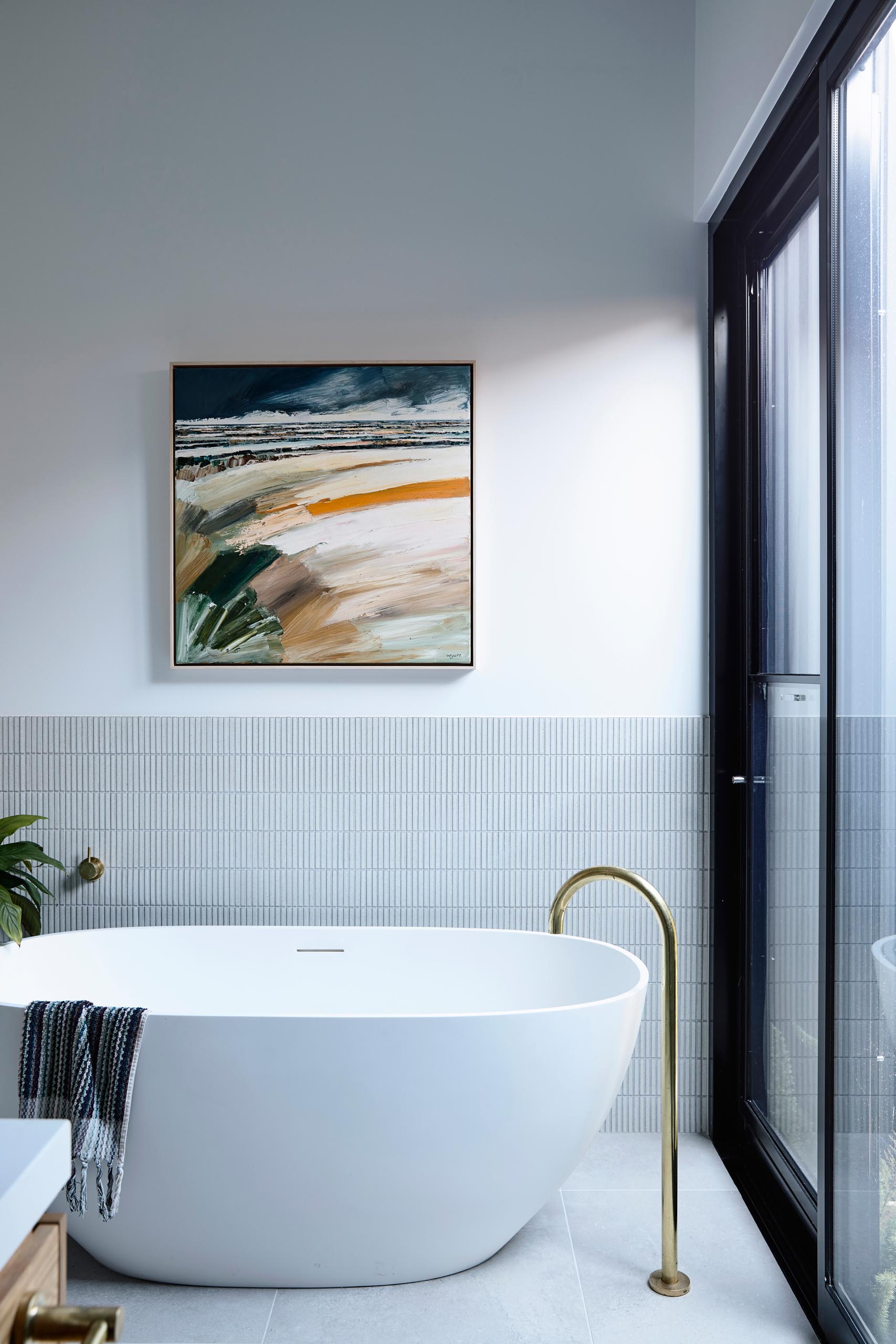 A modern bathroom with a freestanding white bathtub that has a backdrop of small rectangular tiles in a vertical layout.