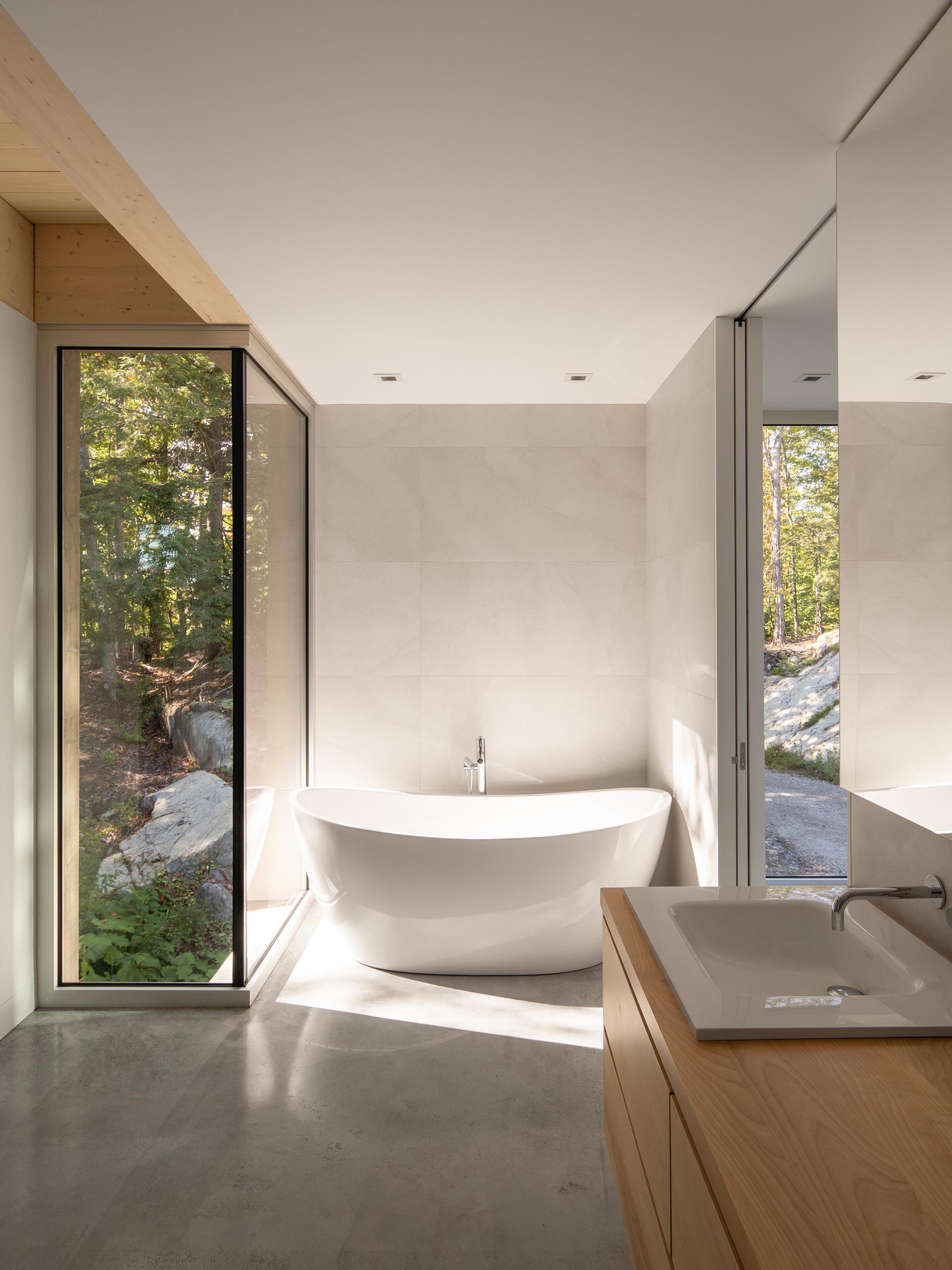 In this modern bathroom, there's a freestanding bathtub with forest views, while a wood vanity adds a natural element.