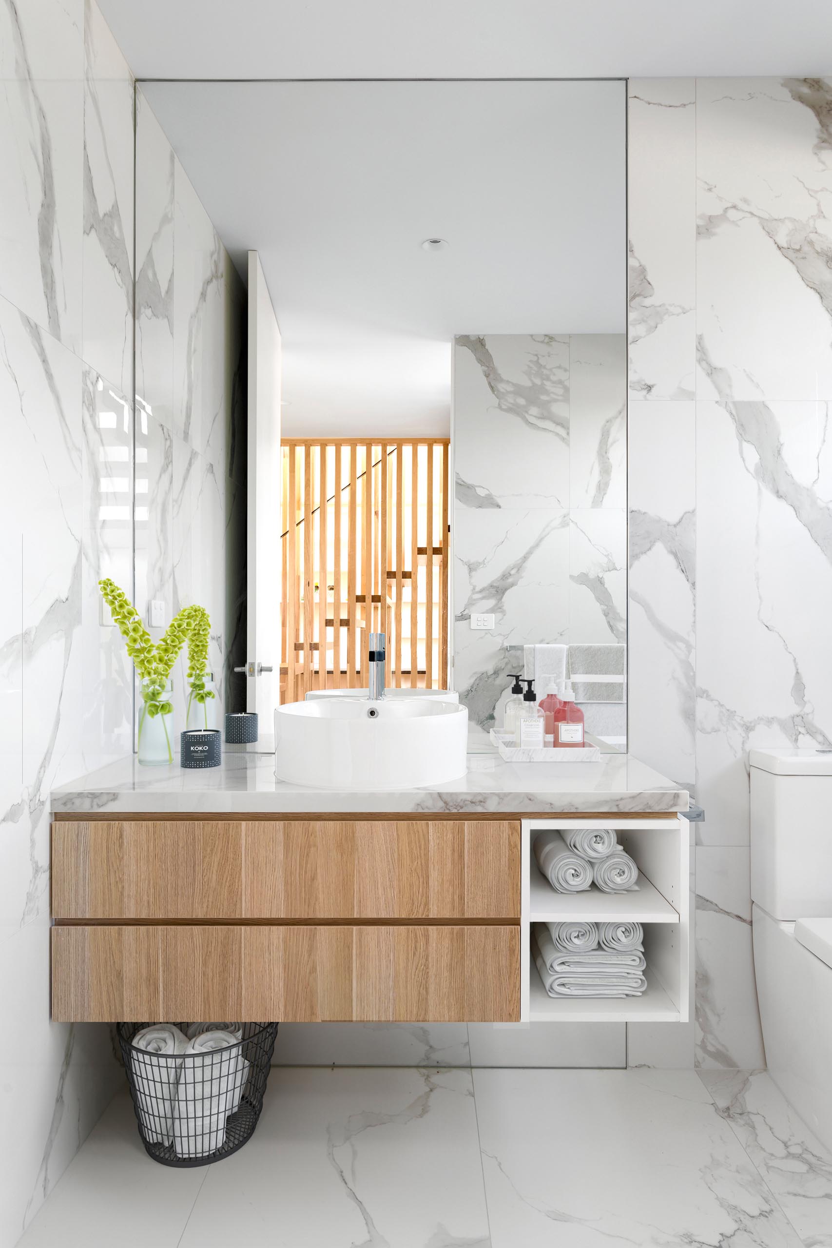 Trong phòng tắm hiện đại này, gạch lát đá cẩm thạch bao phủ tường và sàn, trong khi bàn trang điểm bằng gỗ tạo thêm yếu tố tự nhiên.
