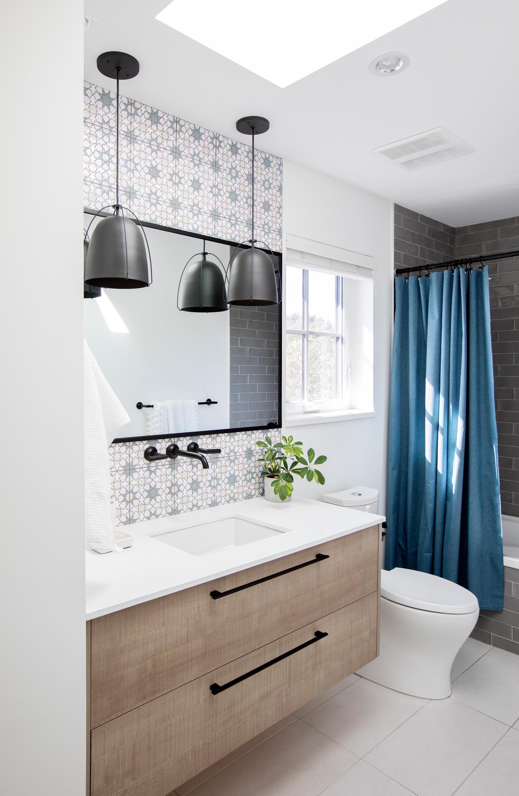 In this modern bathroom, patterned tiles have been used to designate the vanity area, while black pendant lights complement the black mirror frame and shower curtain rod.