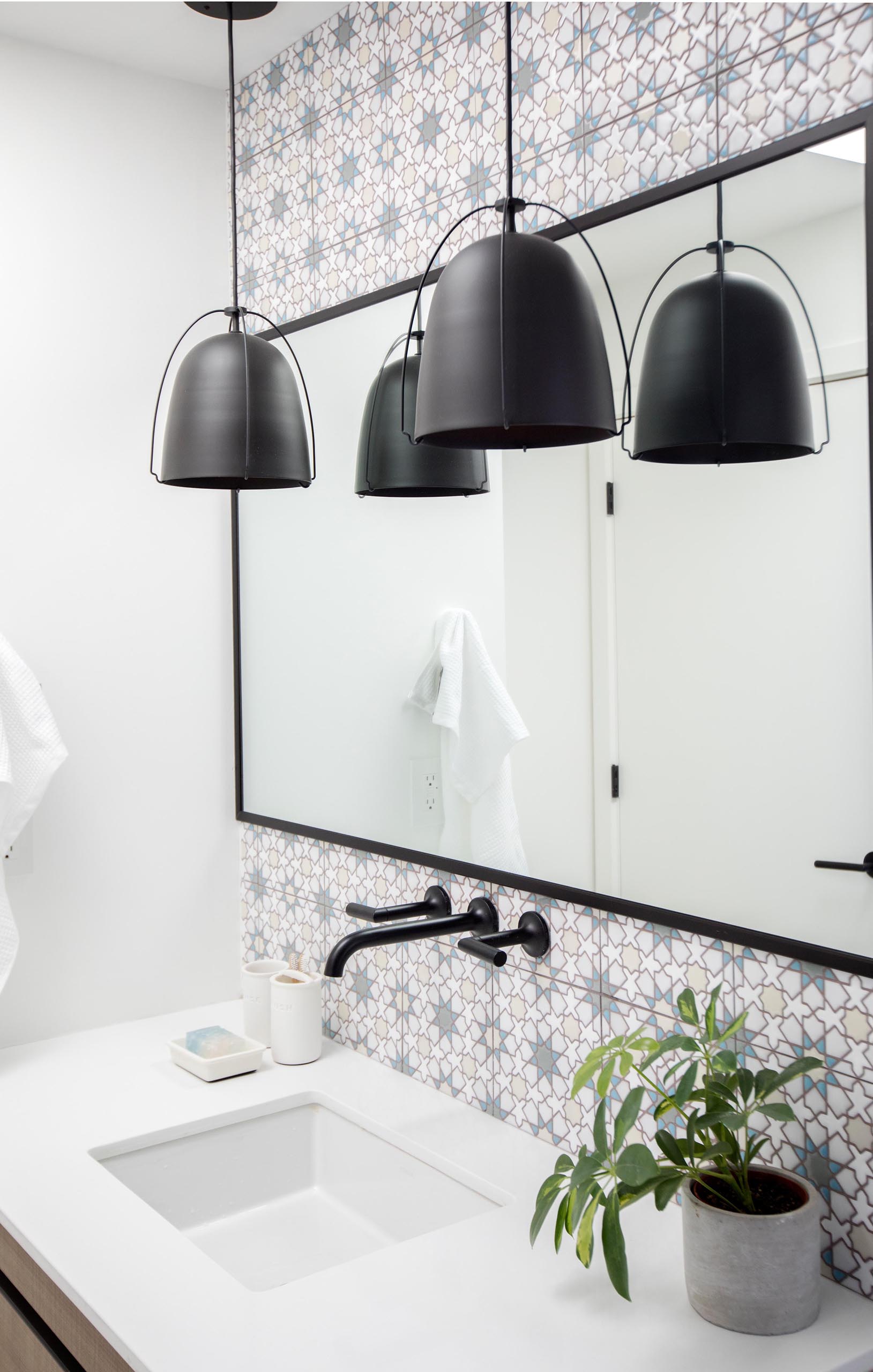 In this modern bathroom, patterned tiles have been used to designate the vanity, while black pendant lights complement the black mirror frame and shower curtain rod.