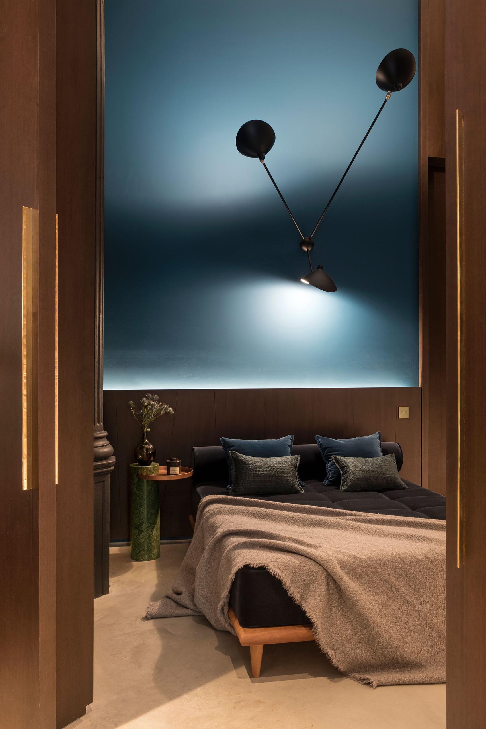 A modern bedroom with high ceilings and a bold matte blue accent wall.