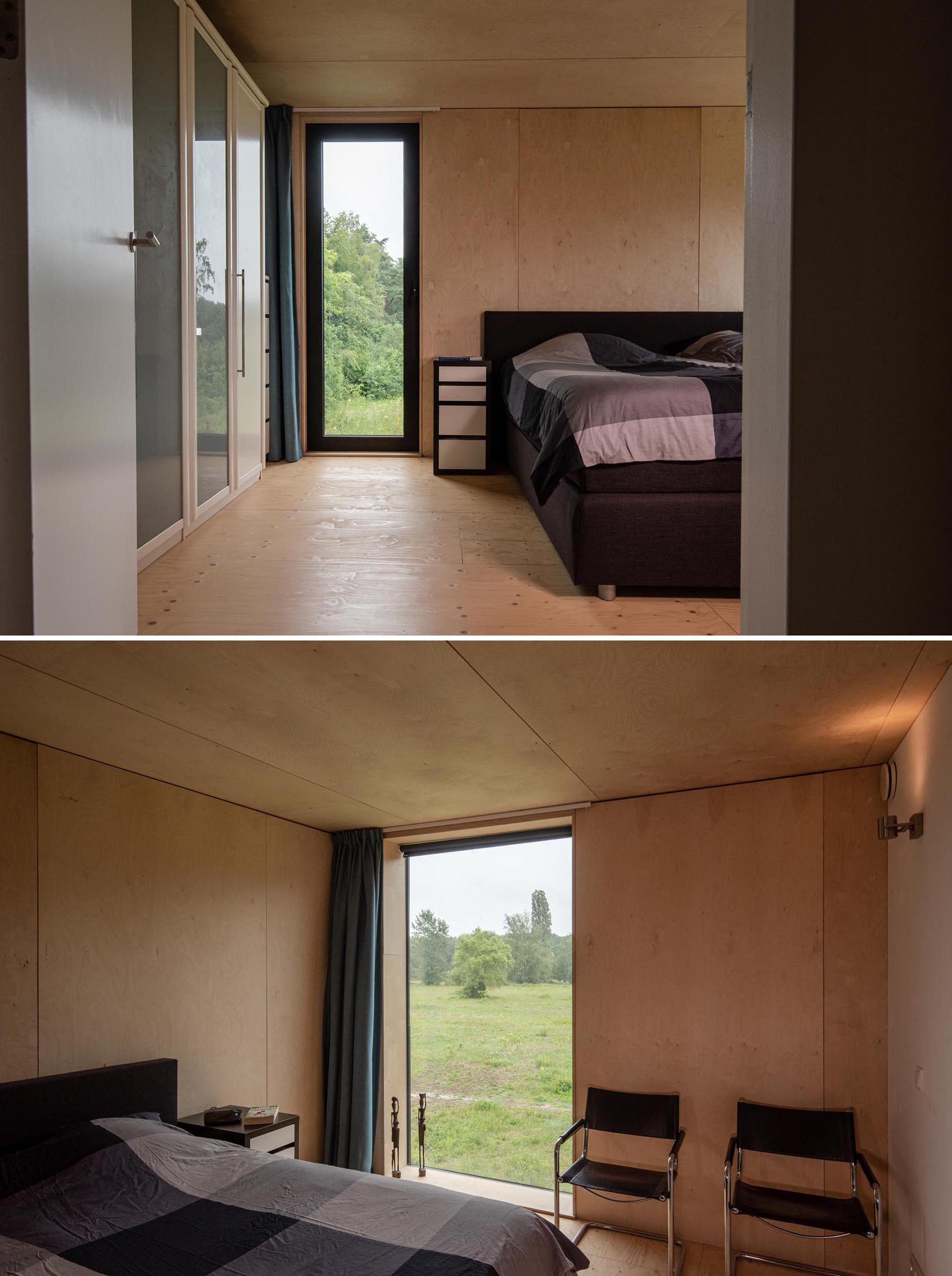 A modern bedroom with plywood walls, and a black bed frame that matches the matte black window frames.