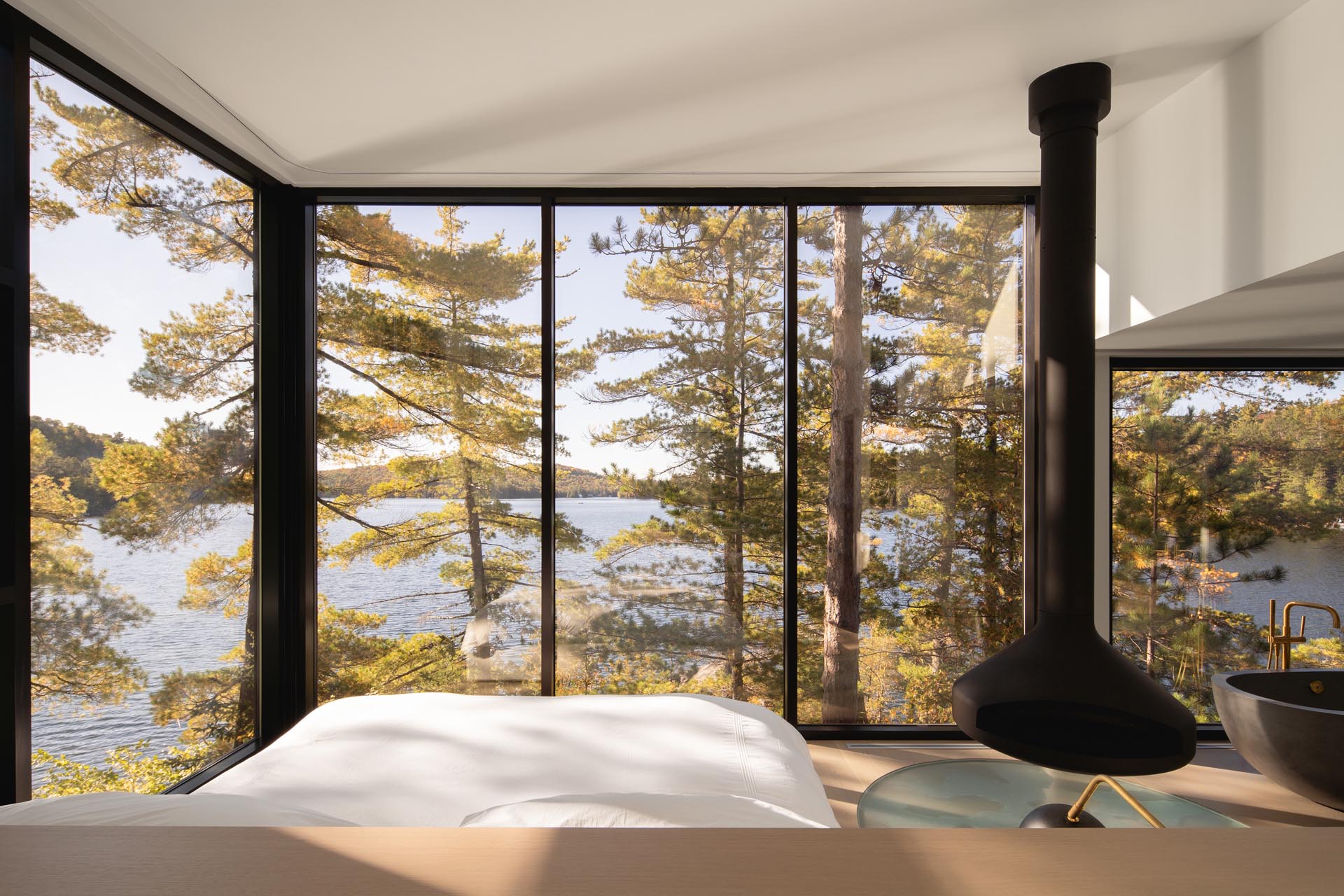 A modern master bedroom with floor-to-ceiling windows, a suspended black fireplace, and a freestanding bathtub.