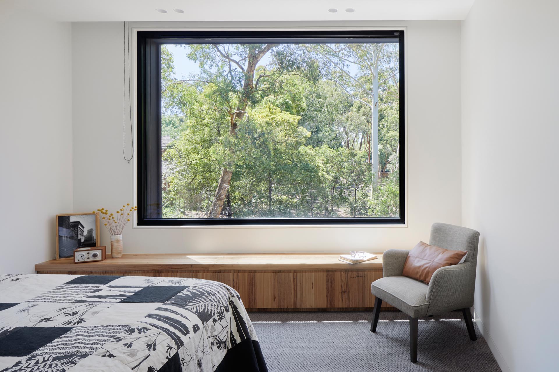 In this modern bedroom, a large window offers views of the gum trees outside, while plush wool carpet helps to absorb sound for privacy.