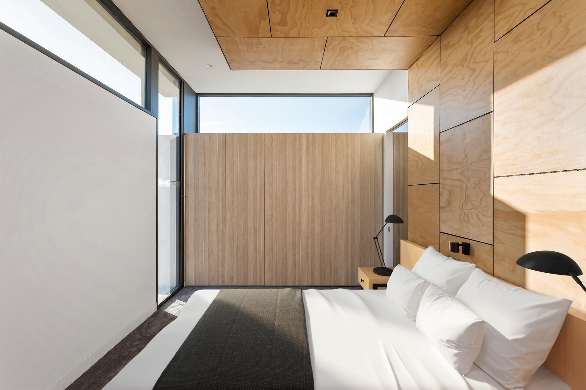 Trong phòng ngủ hiện đại này, cửa sổ khe đổ bóng mỏng lên bức tường nổi bật phía sau giường, đồng thời tăng thêm sự riêng tư.