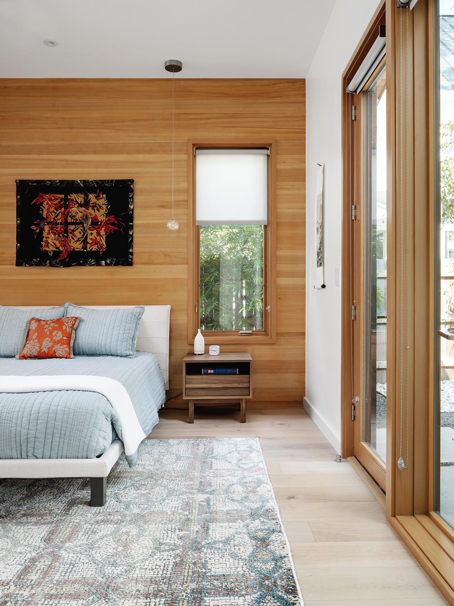 A modern bedroom with light blue bedding and a wood accent wall.