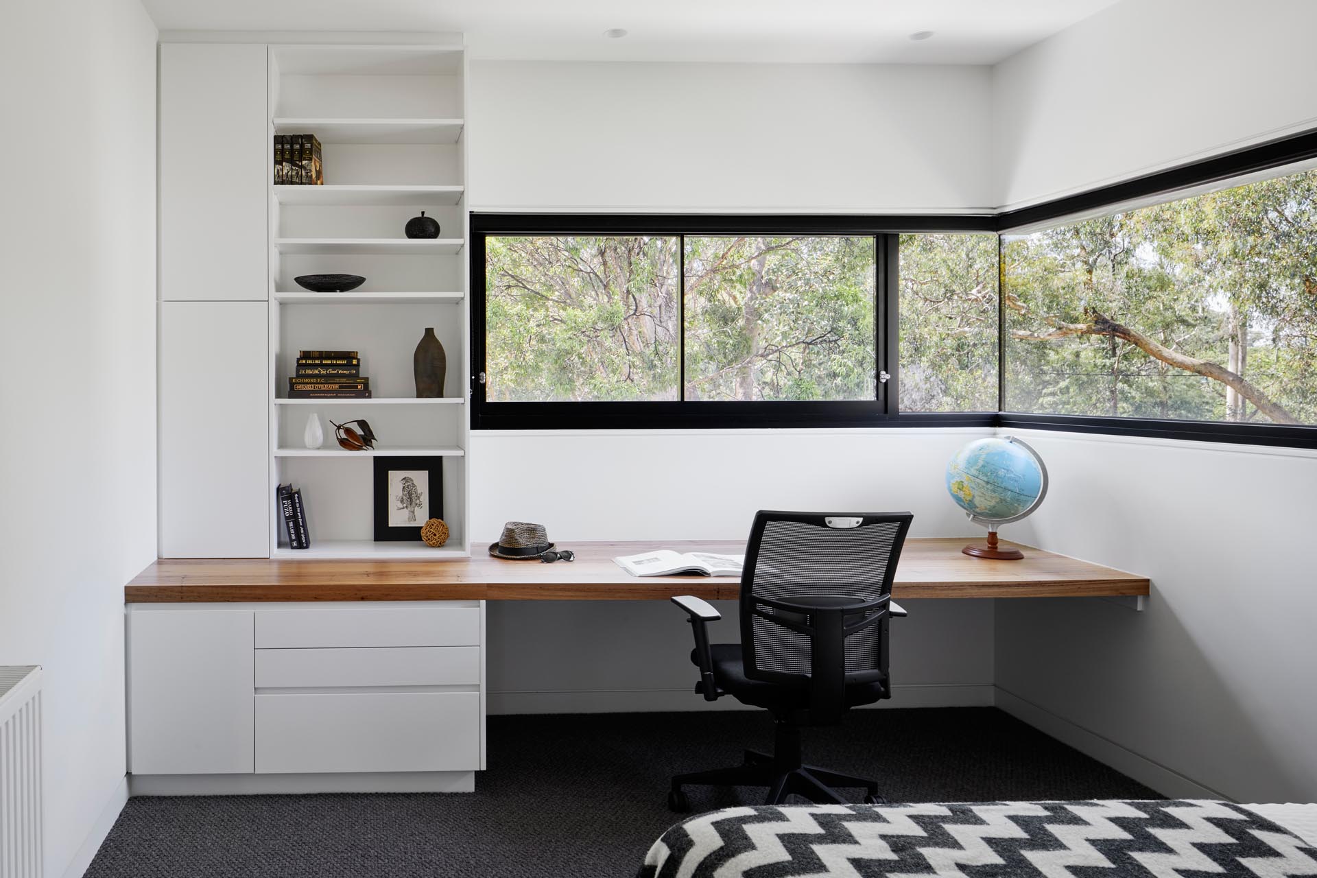 In this modern bedroom, there's wrap-around windows and a built-in wood desk with drawers, cabinets, and shelving.