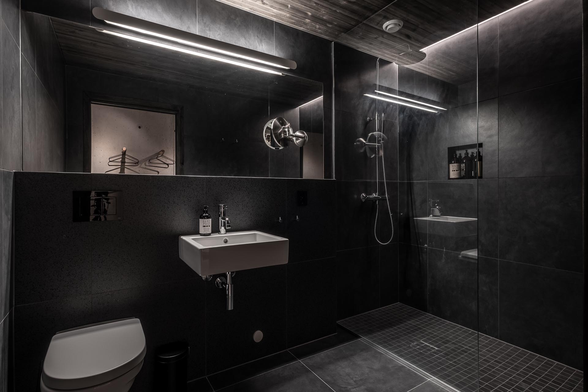 In this dark bathroom, large format black tiles and lighting have been used to create a dramatic appearance.