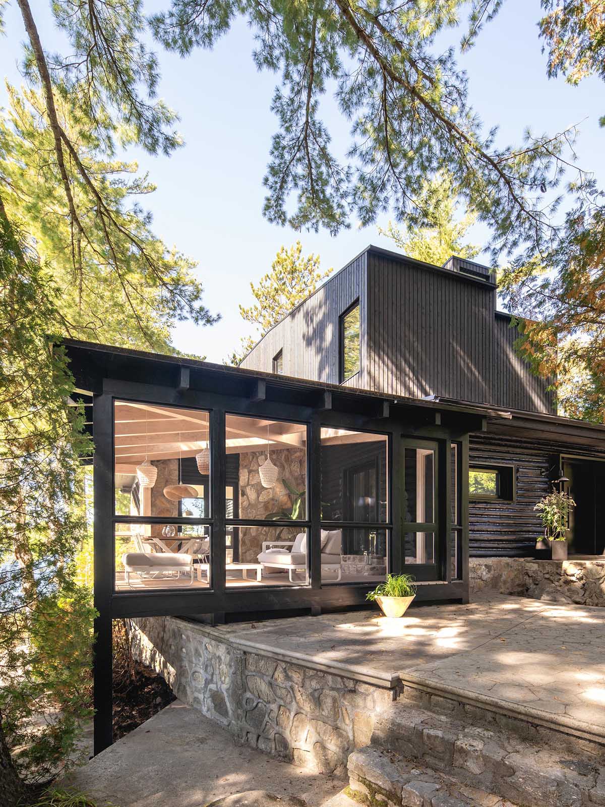 A log cabin with a stone foundation has a modern extension and screened-in porch.