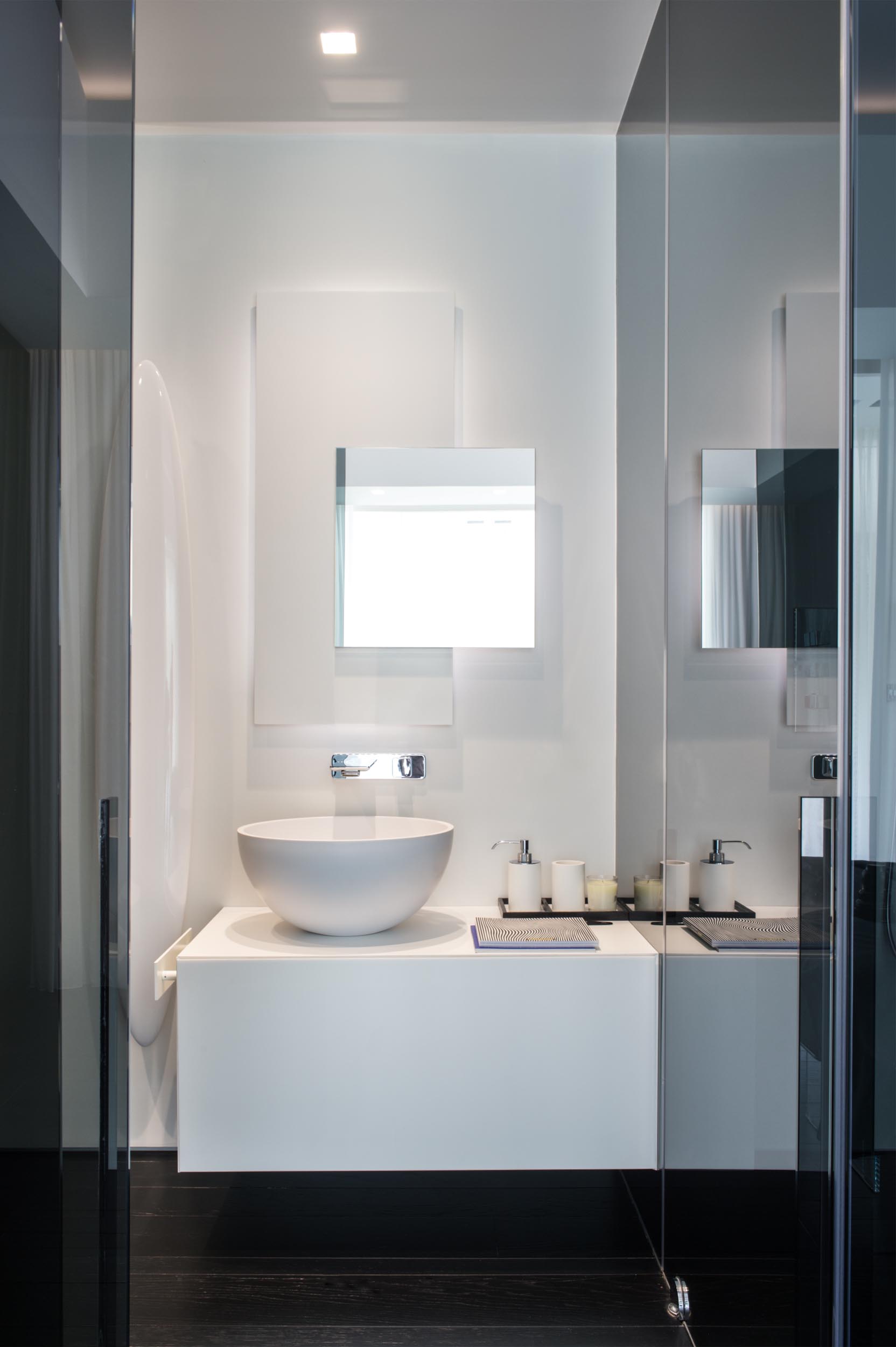 A modern bathroom with a white vanity and backlit mirror, and contrasting black floor.