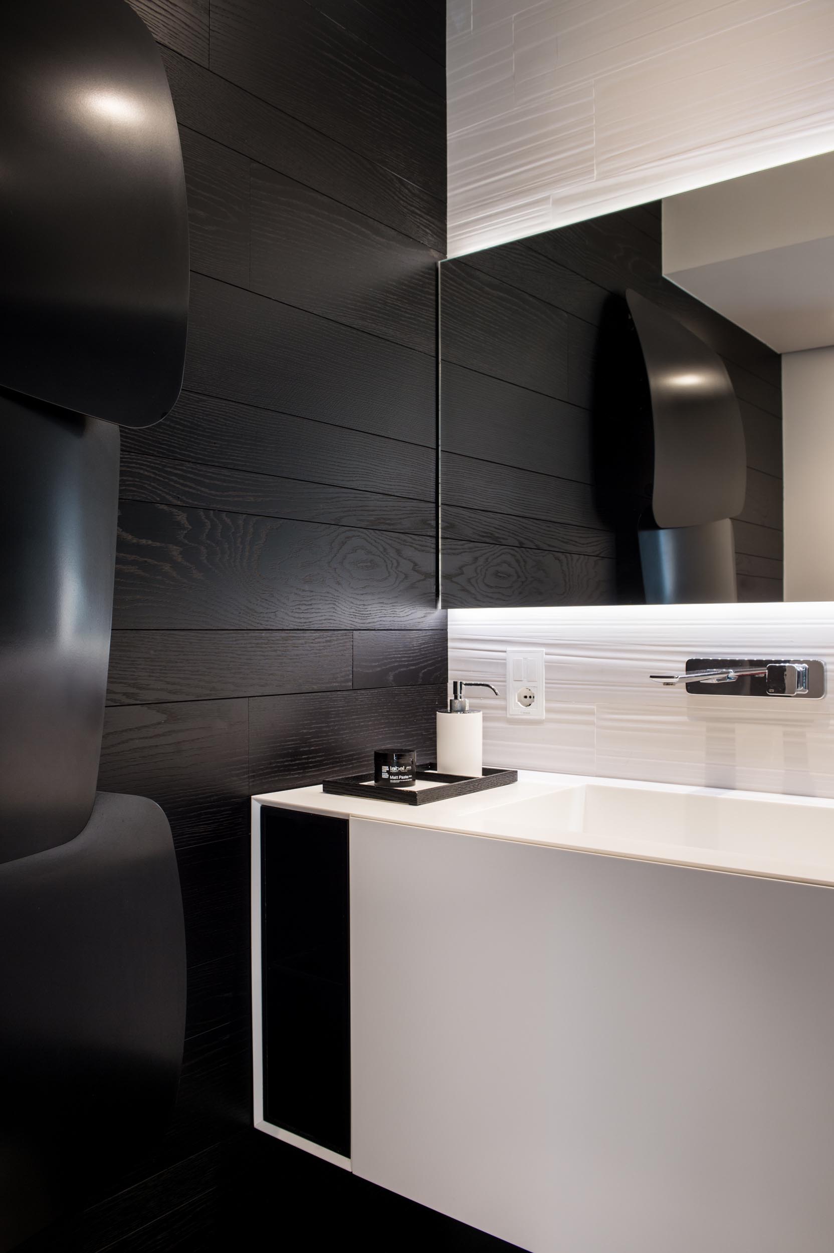 A modern bathroom with a white vanity and backlit mirror, and a contrasting black accent wall.