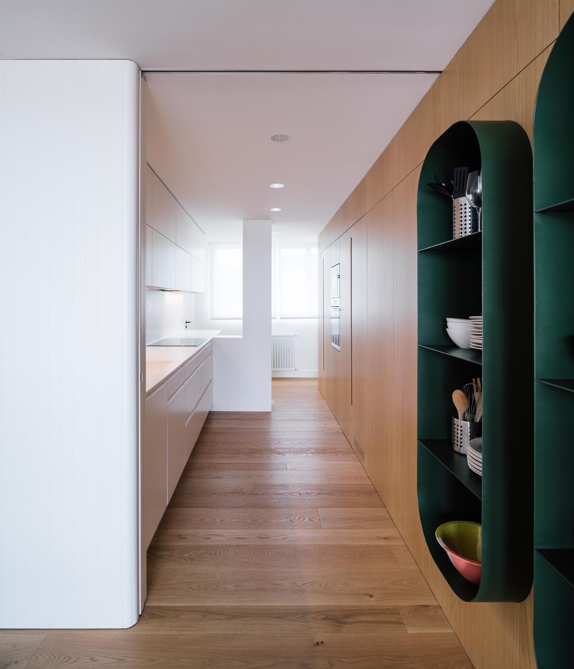 A modern white kitchen with a wall of storage made from wood.