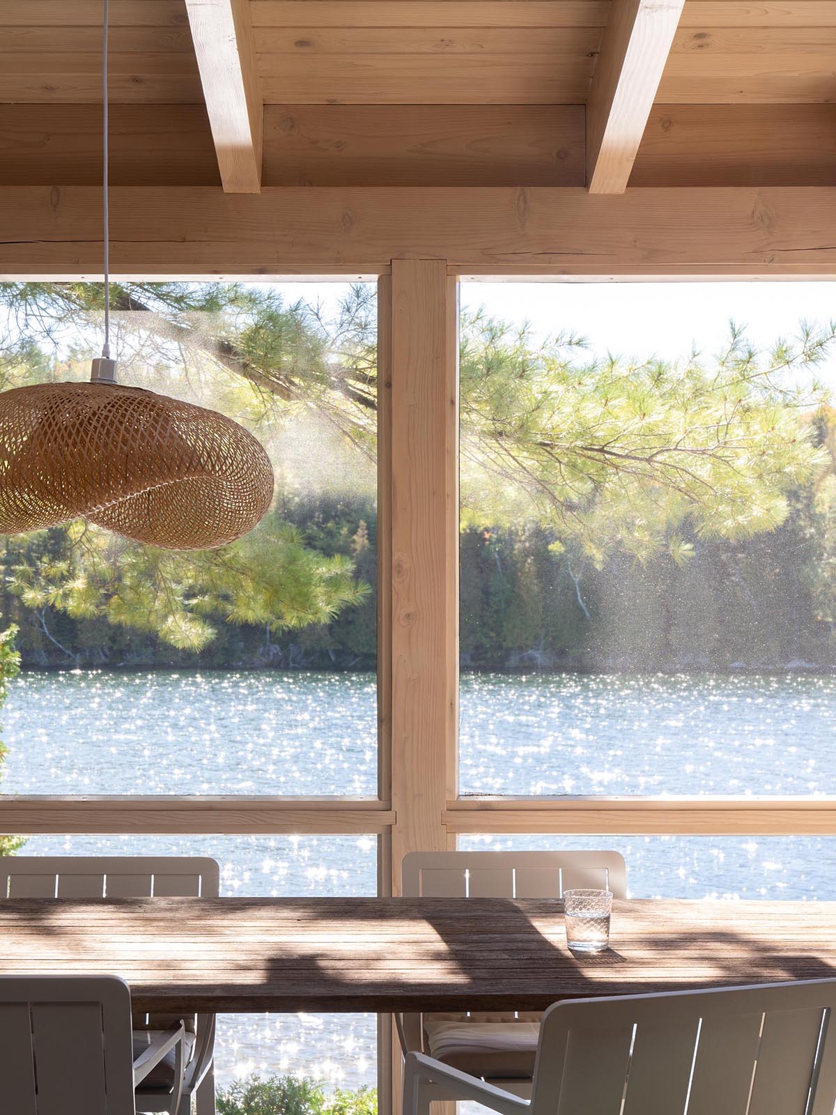 This modern cabin has a set of doors that open to a screened in porch, that's furnished with a dining table and a sofa with matching bench.