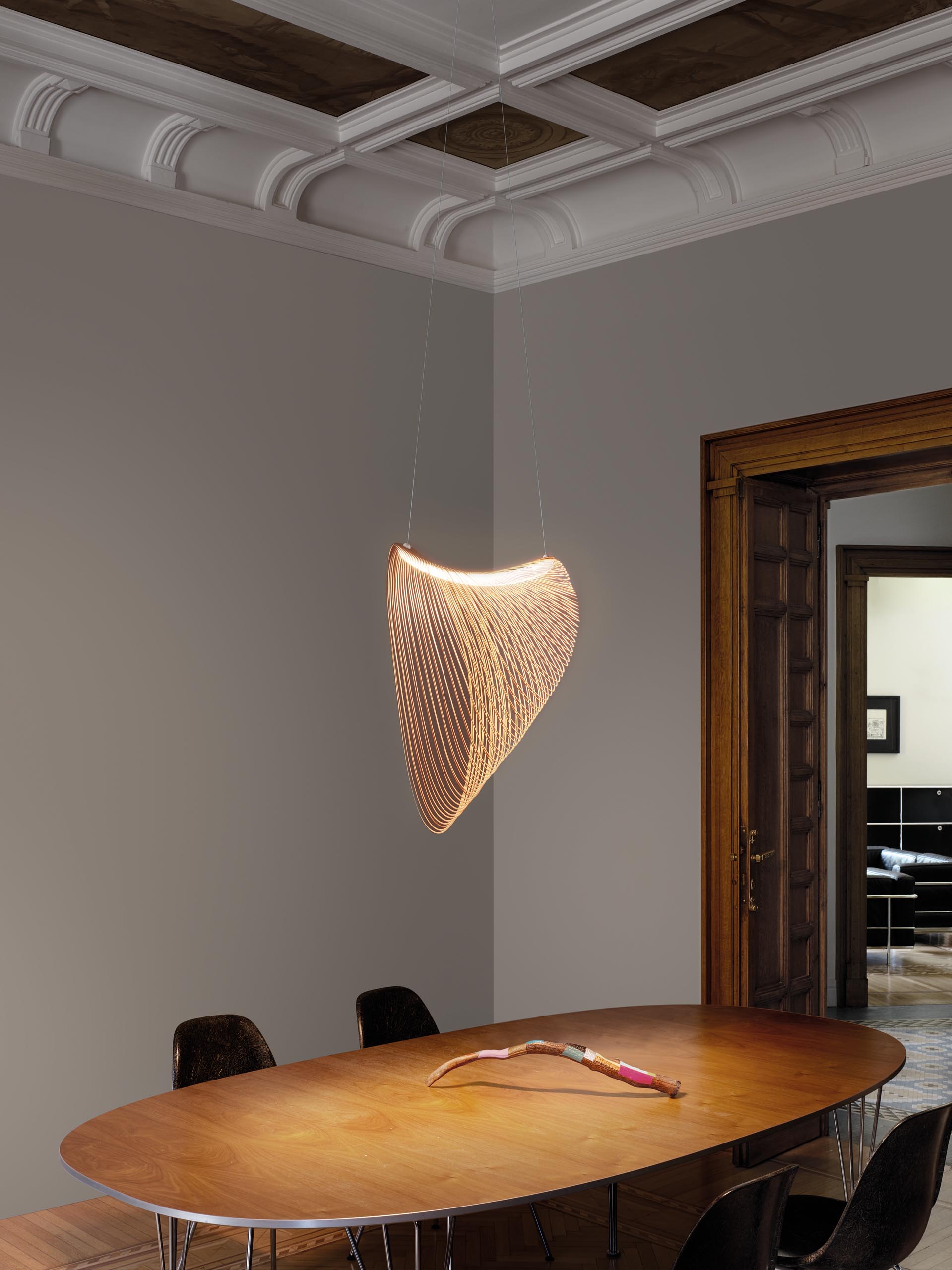 A delicate pendant light made from laser cut wood and LEDs hangs above a dining table..