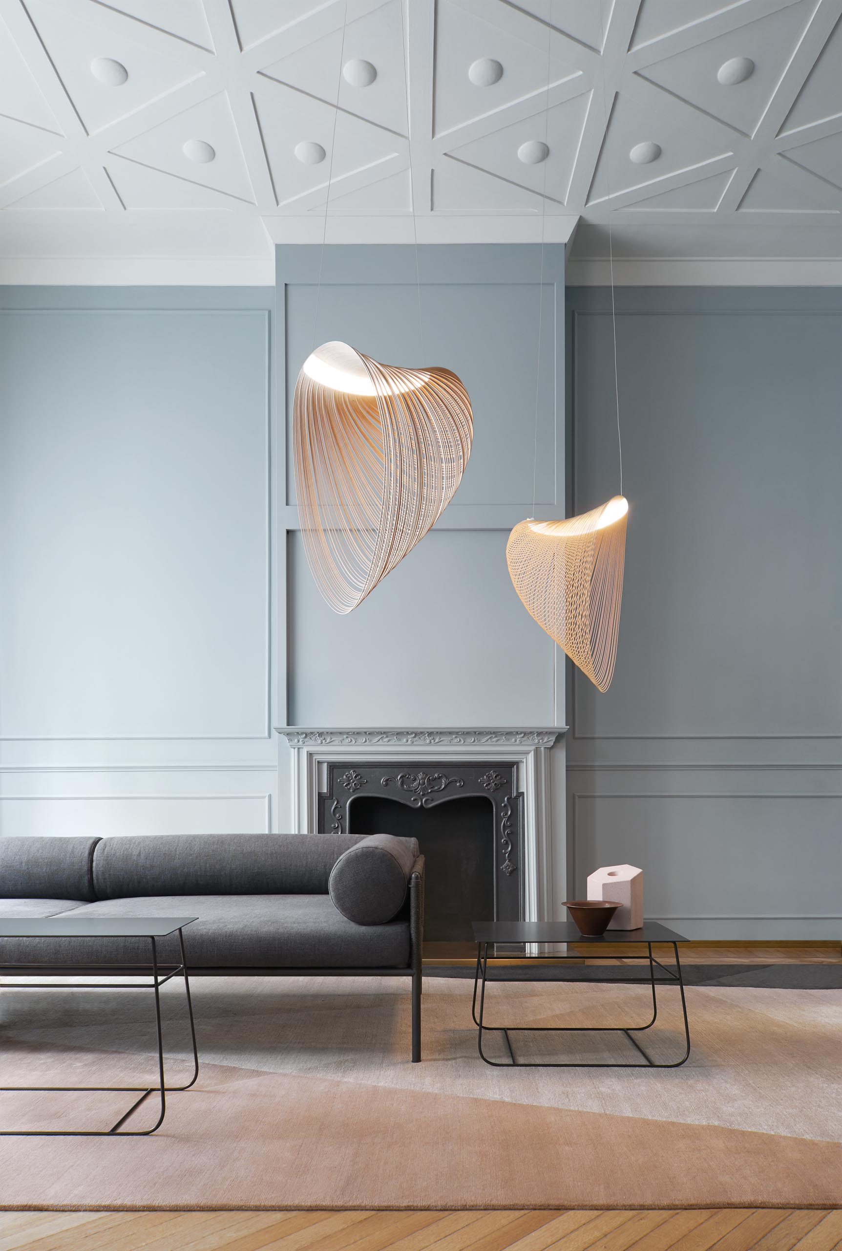 A pair of delicate and sculptural pendant light hang in a living room.