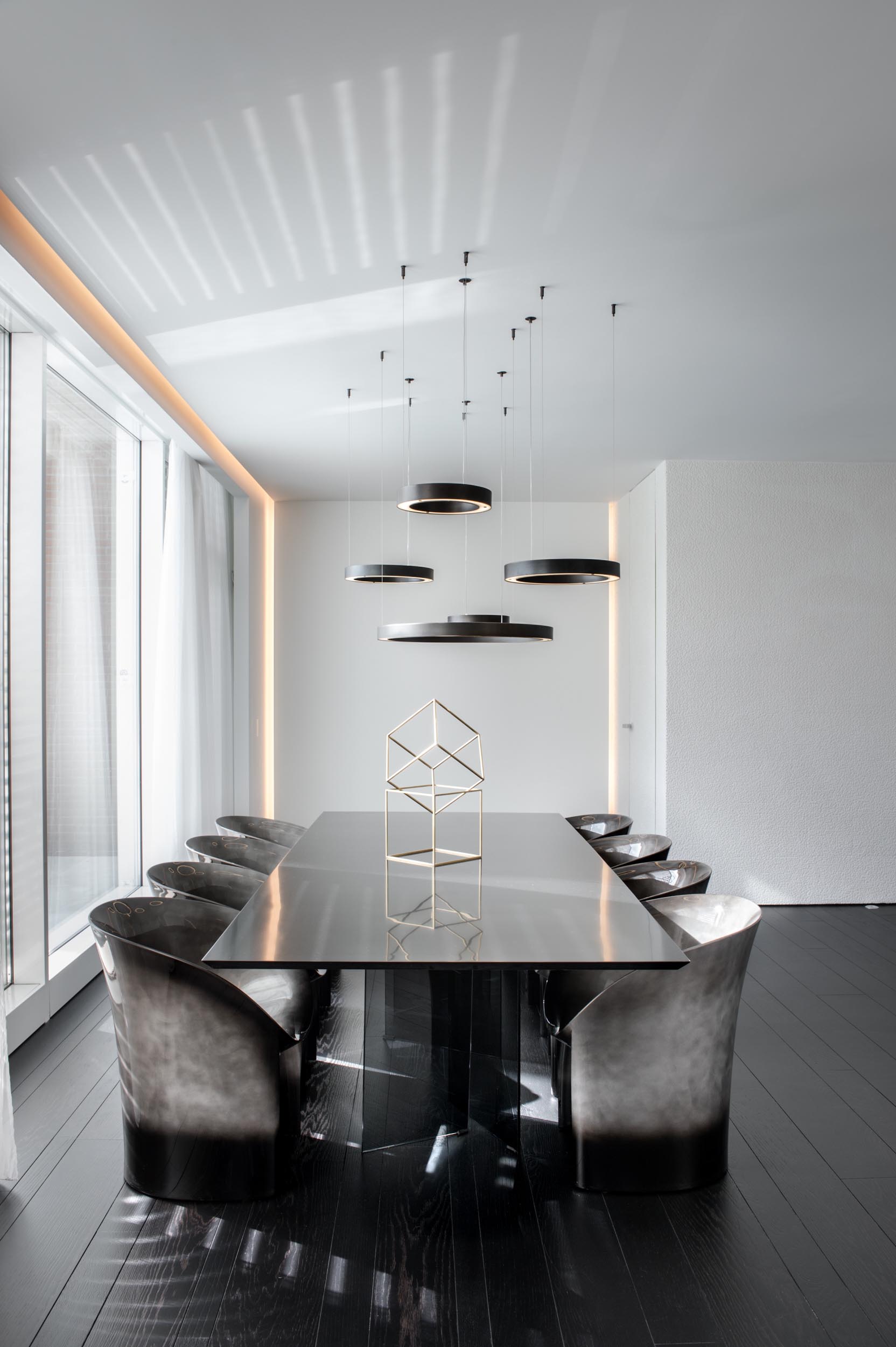 A modern dining room with circular pendant lights hanging above the black dining table, while the surrounding dining chairs are dark with a silvery element.