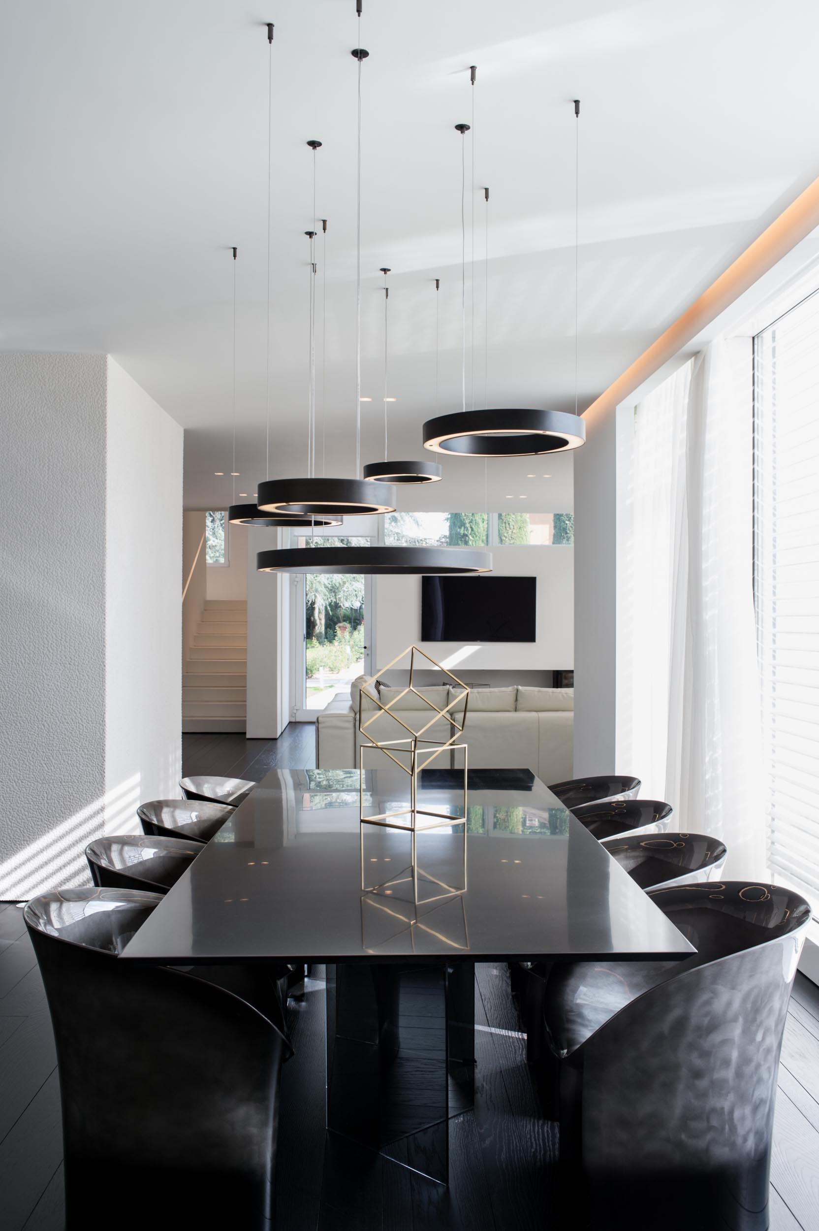 A modern dining room with circular pendant lights hanging above the black dining table, while the surrounding dining chairs are dark with a silvery element.