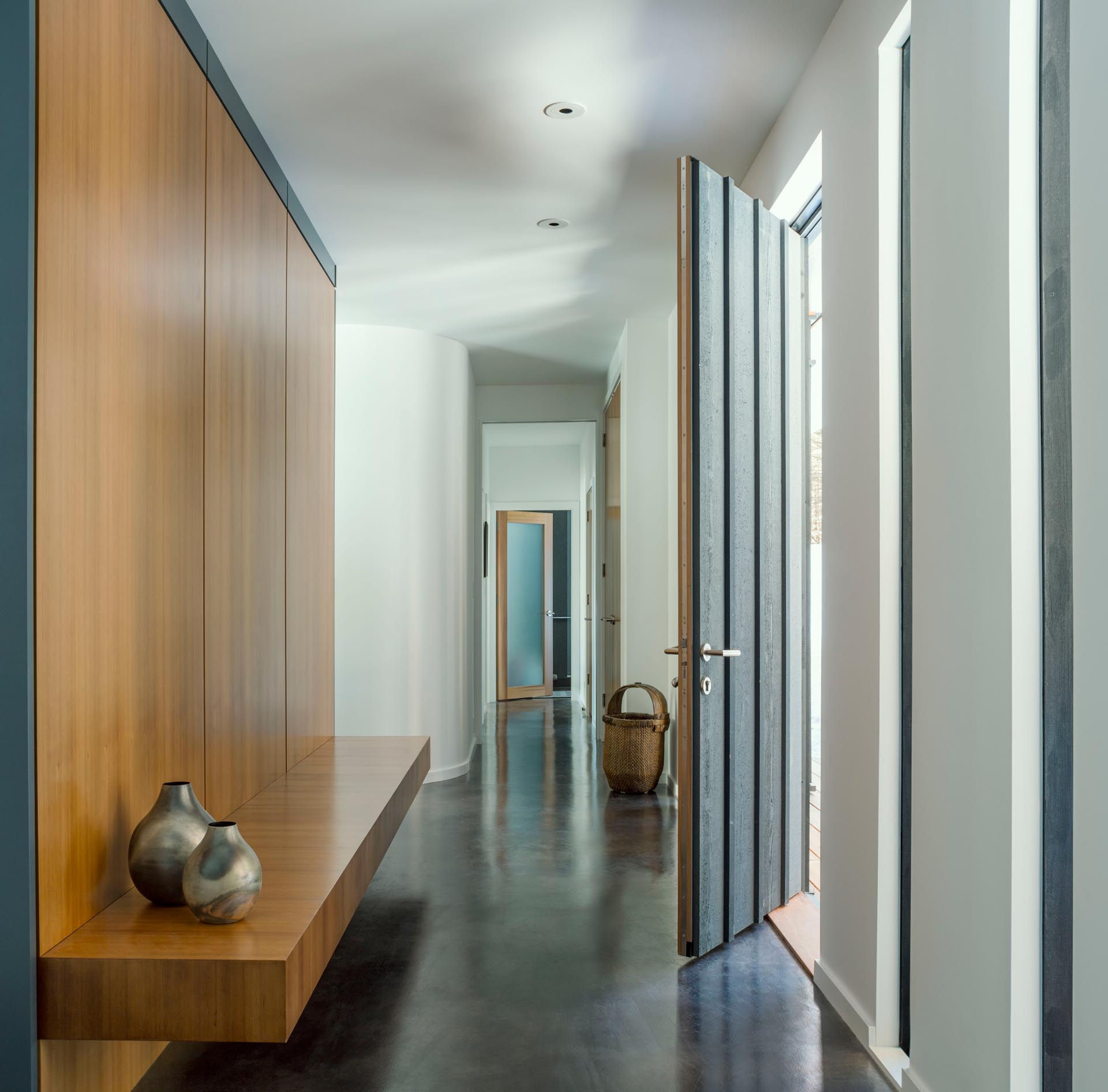 A modern entryway with polished concrete floor, a wood accent wall, and a floating wood bench.