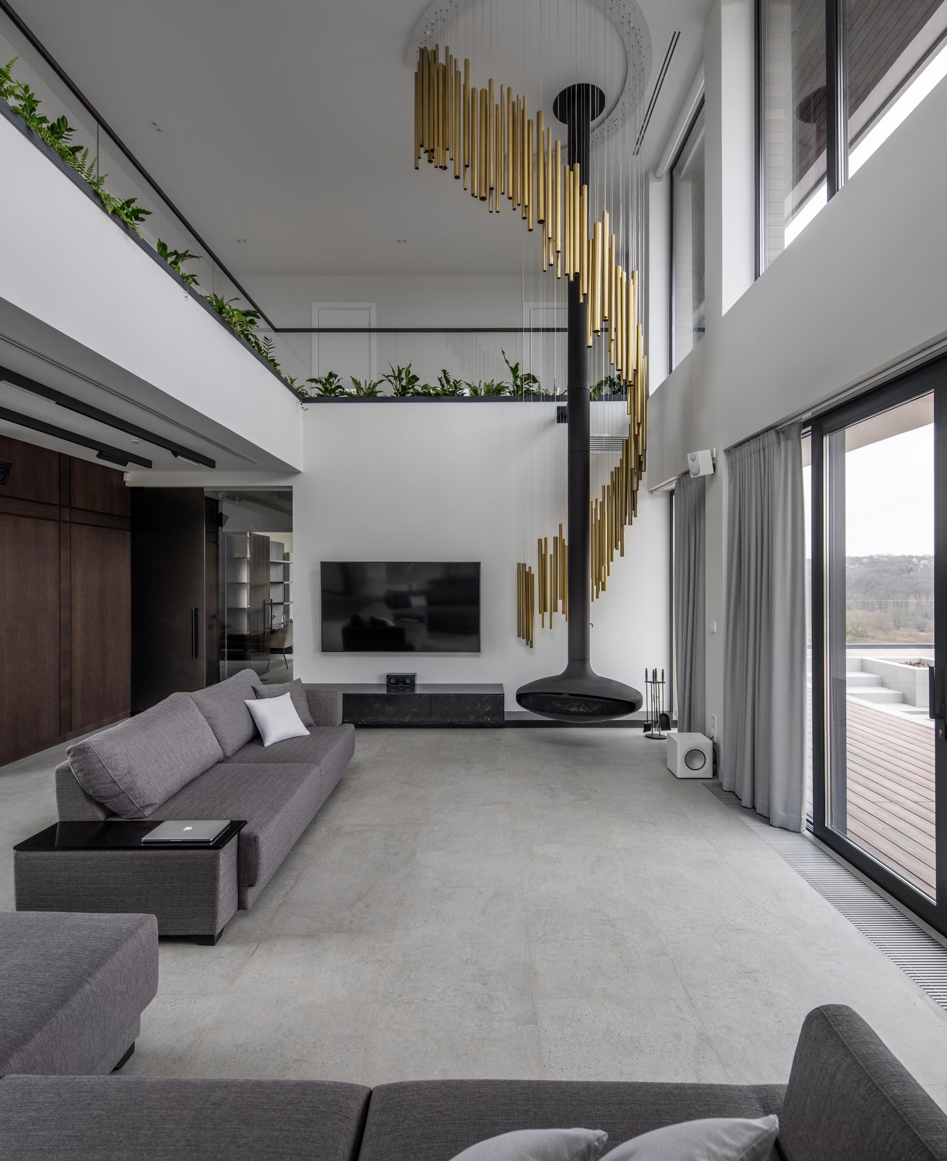 A modern living room with a suspended black fireplace and a sculptural lamp made from brass tubes whose design was inspired by wind chimes. 