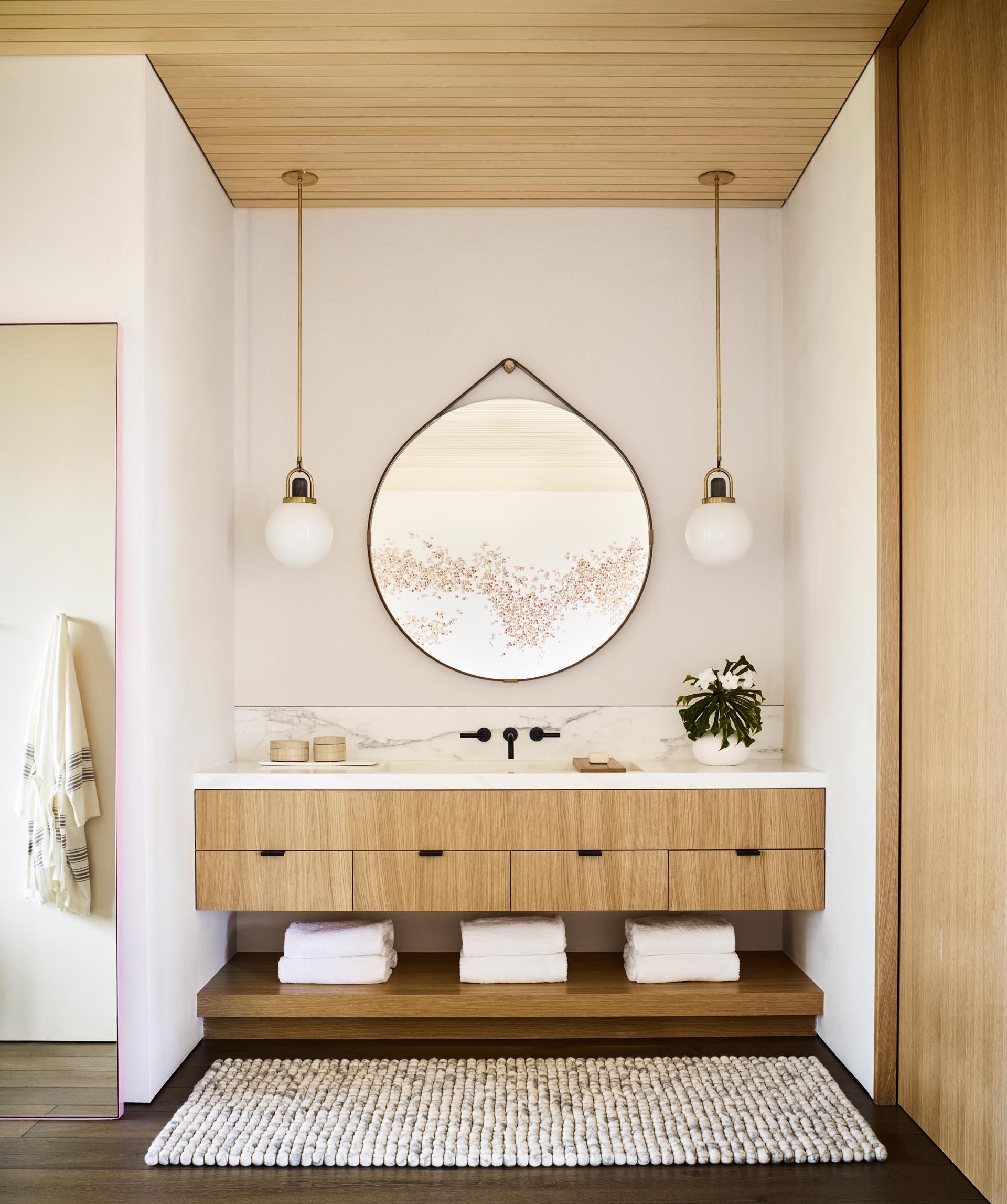 A modern bathroom with a natural color palette, a light wood vanity, and round hanging mirror.