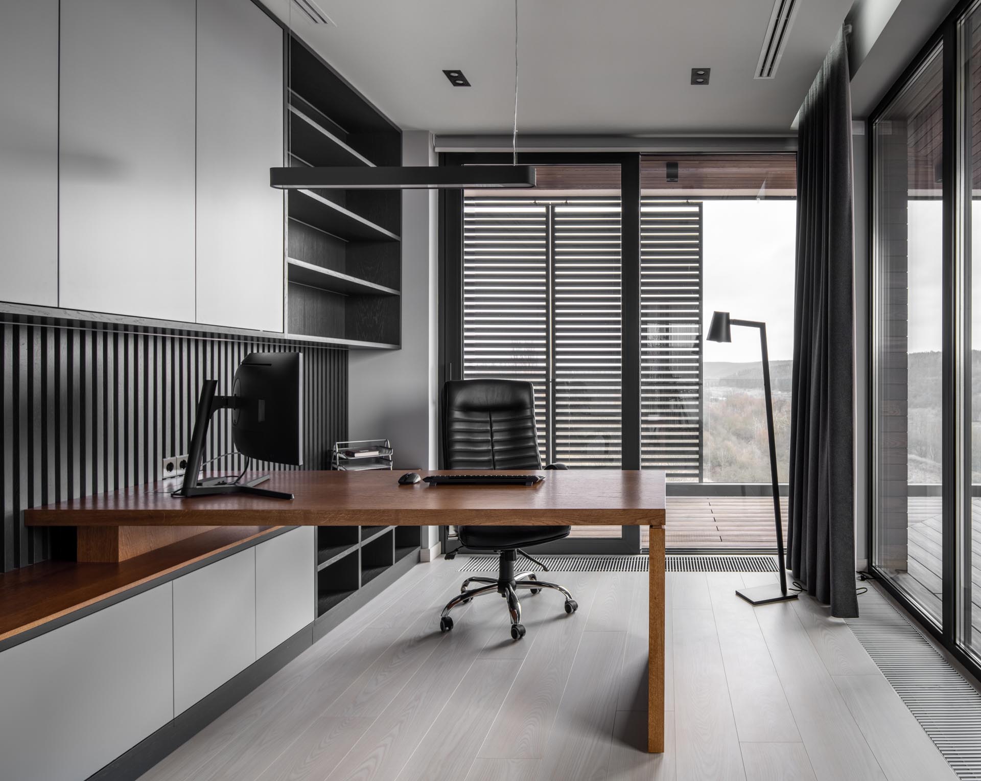 A home office has floor-to-ceiling windows and a built-in cabinetry that incorporates a wood desk.