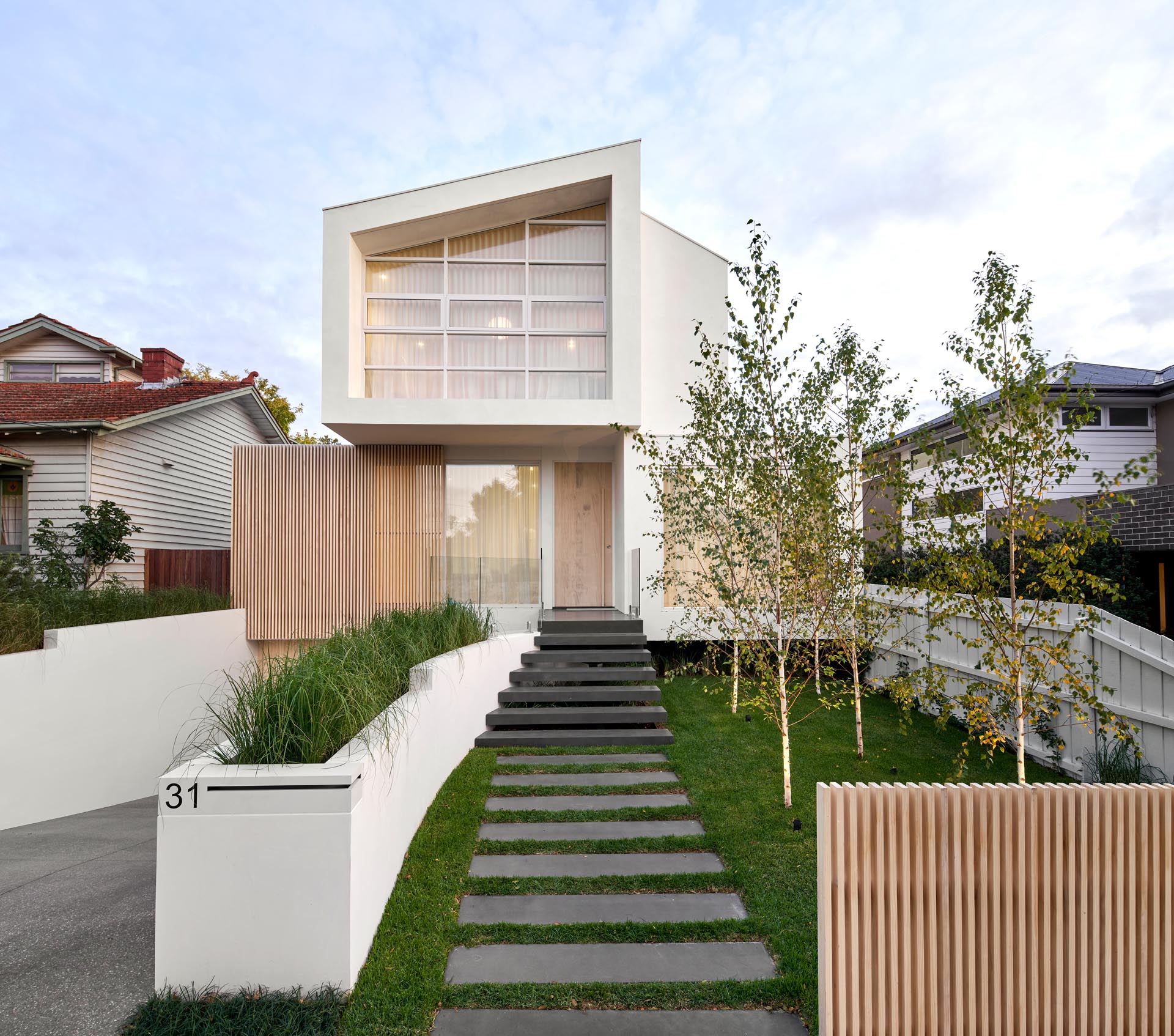 From the street, this house exterior has a path that transforms into steps that lead to the front door, while the driveway and garage are slightly hidden from view by a custom-designed planter.