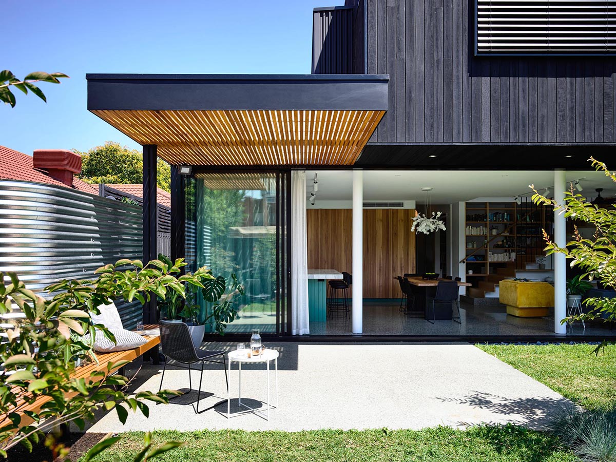 A modern home with a simple pergola that provides partial shade to a patio with a built-in bench.