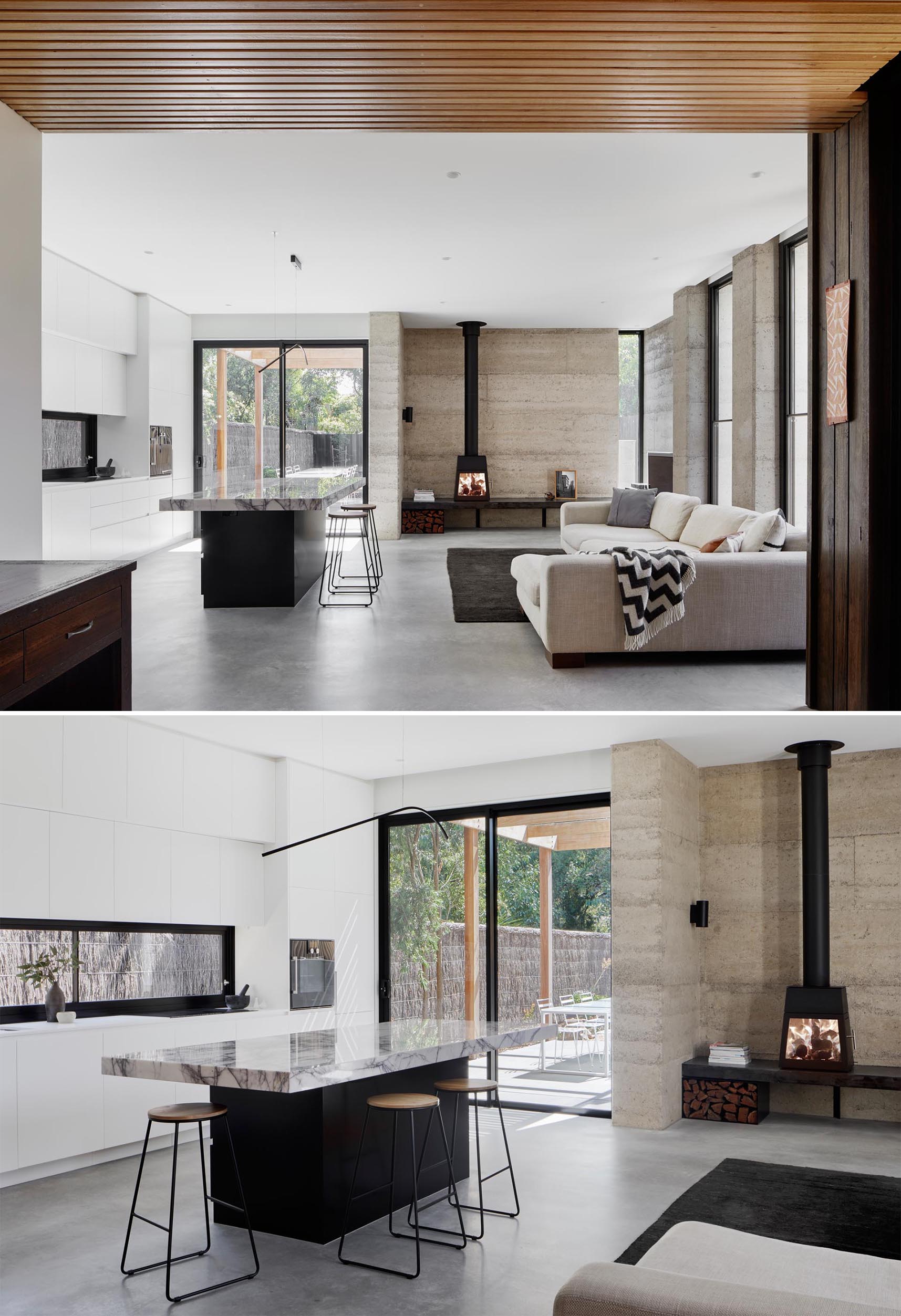 In this modern open plan living room and kitchen, there's a rammed earth wall behind the fireplace and concrete floors.