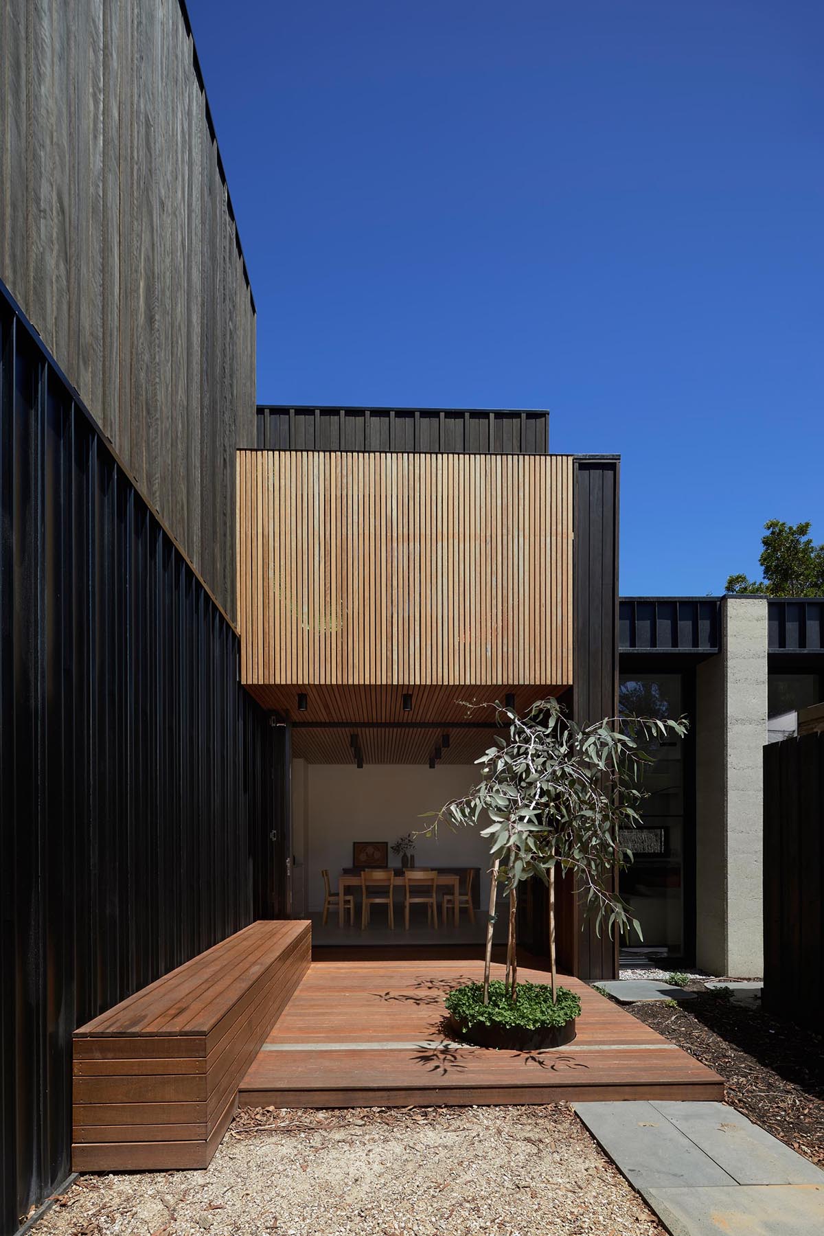 A modern home with dark wood and concrete exterior, and a deck with built-in bench made from lighting wood.