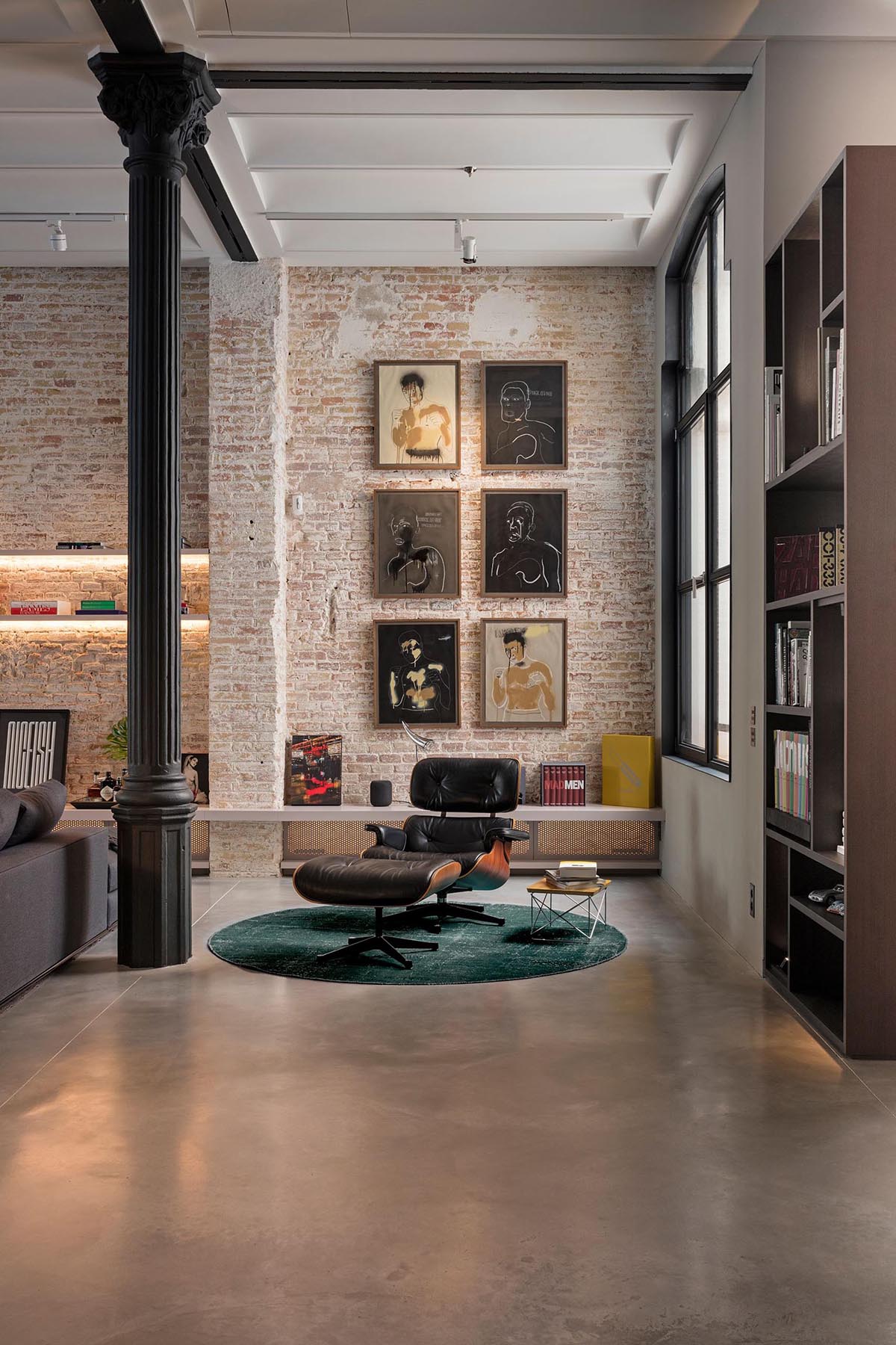 A modern reading nook with high ceilings, a bookshelf, and a single lounge chair and ottoman.