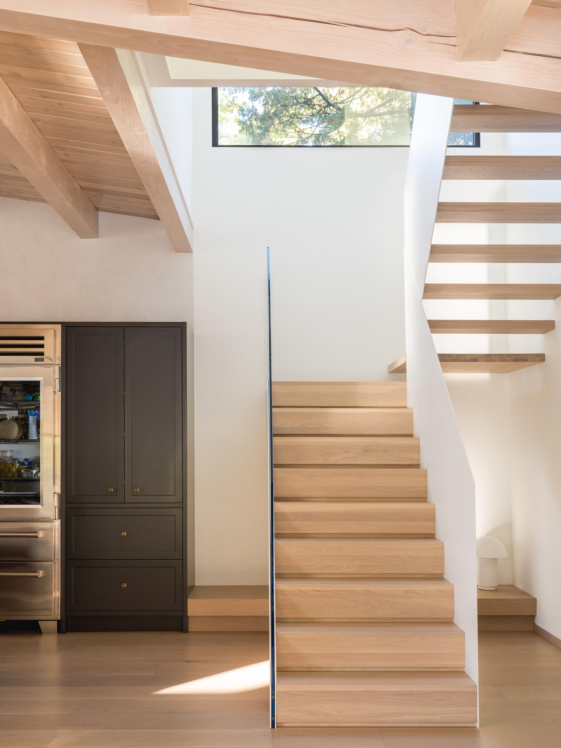 Modern white stairs with wood treads and a glass handrail. 