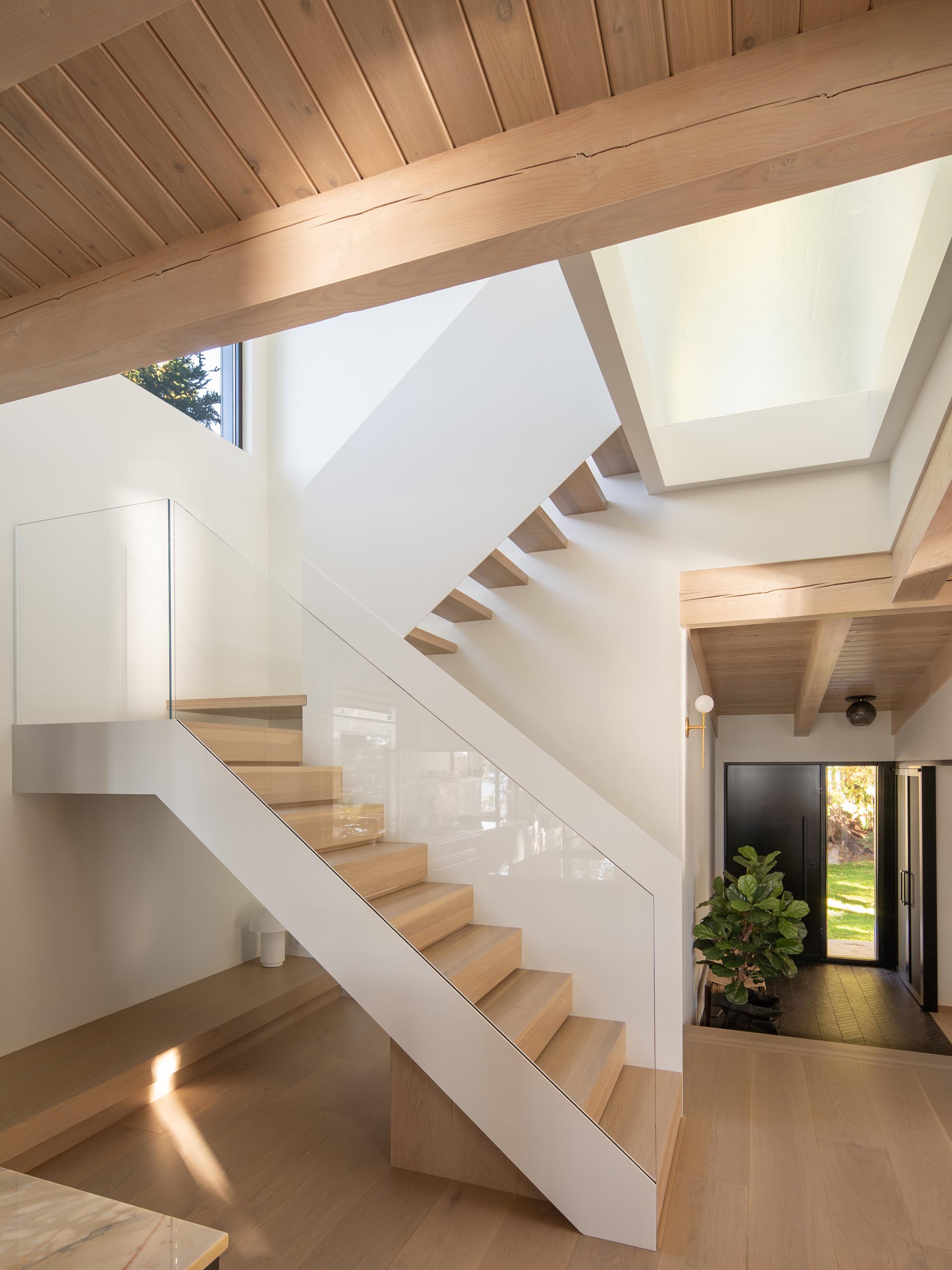 Modern white stairs with wood treads and a glass handrail. 