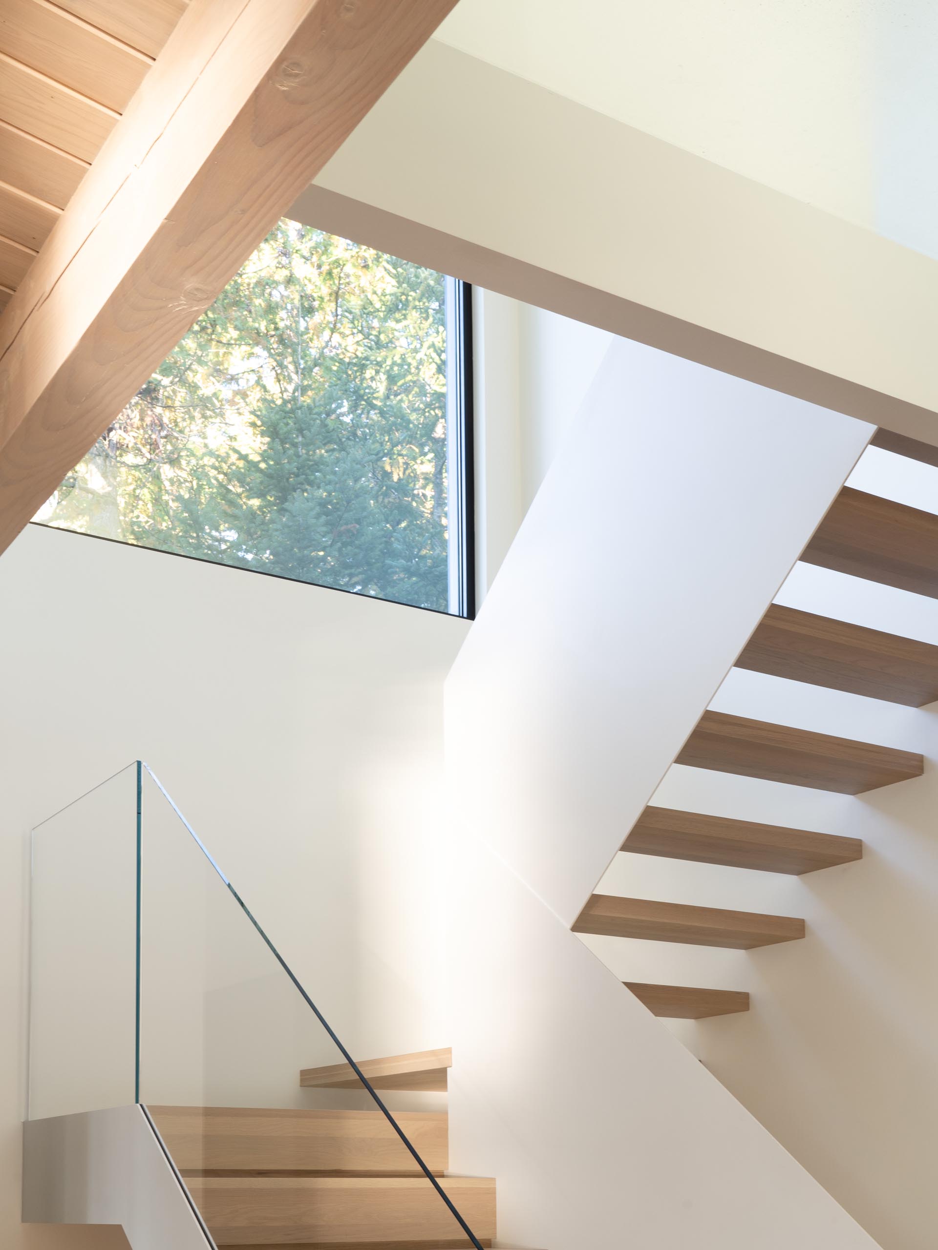 Modern white stairs with wood treads and a glass handrail.