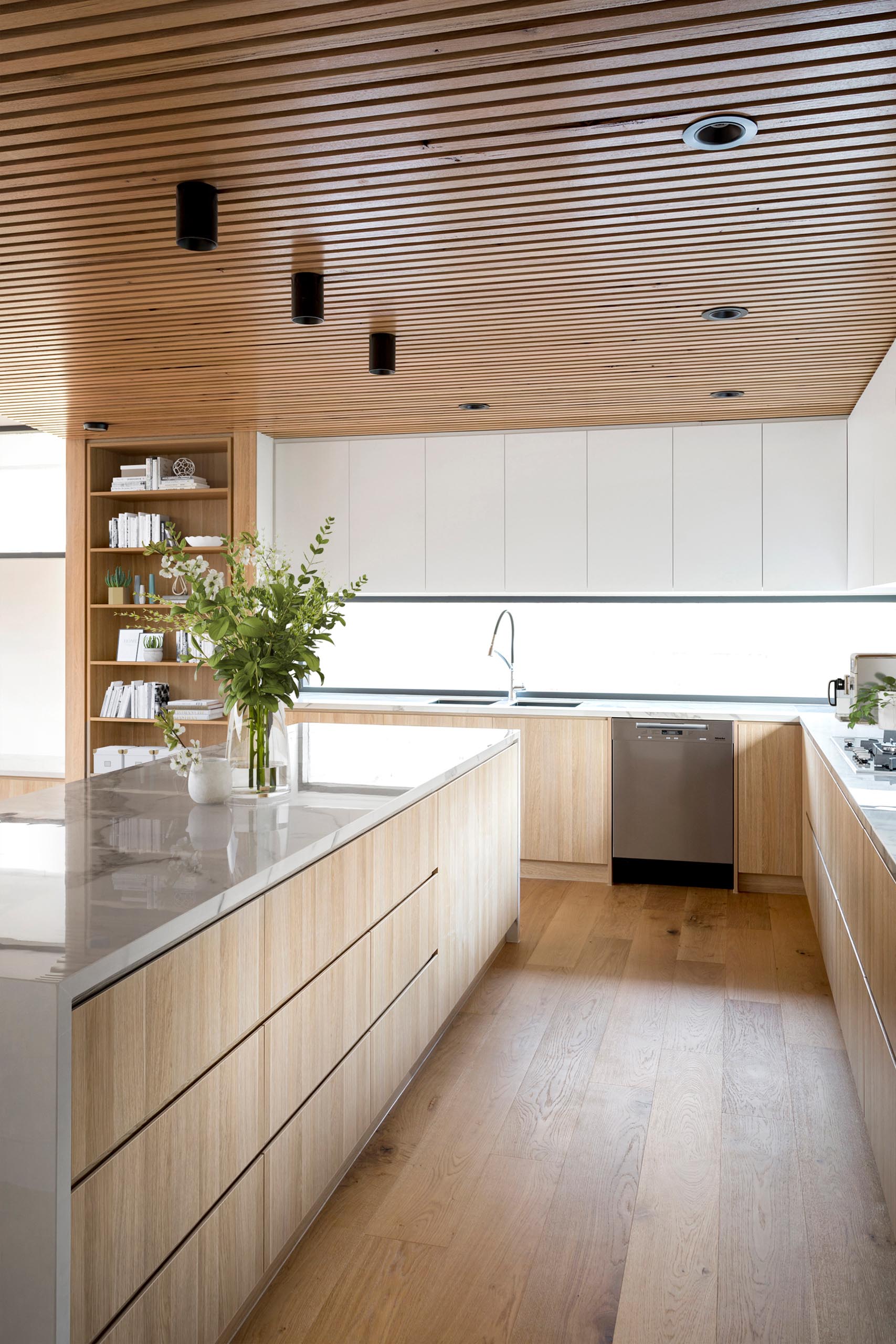 A modern kitchen with a wood ceiling, minimalist cabinets, and a marble island.