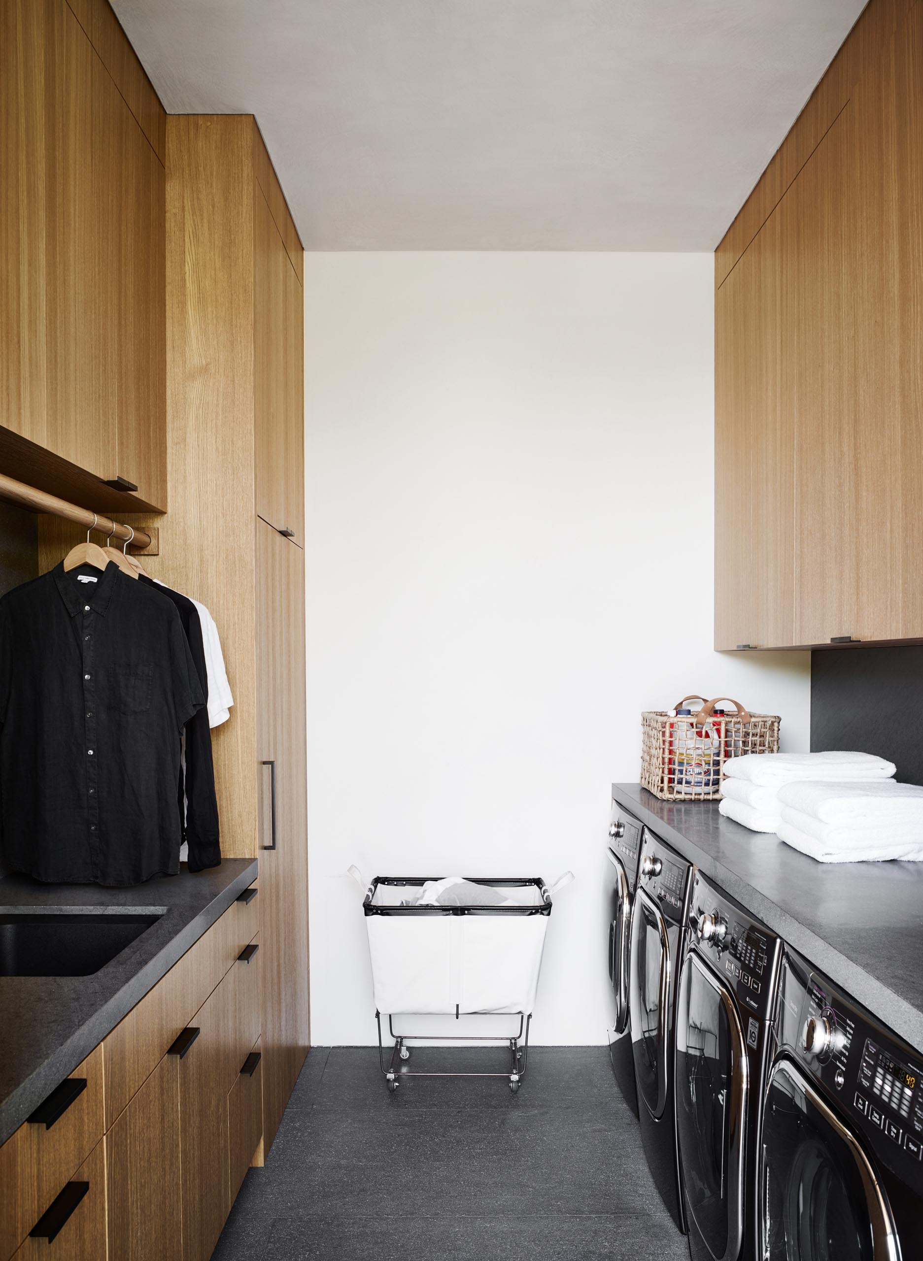 A modern laundry room with floor-to-ceiling wood cabinets, gray countertops, and matching gray floor tiles.