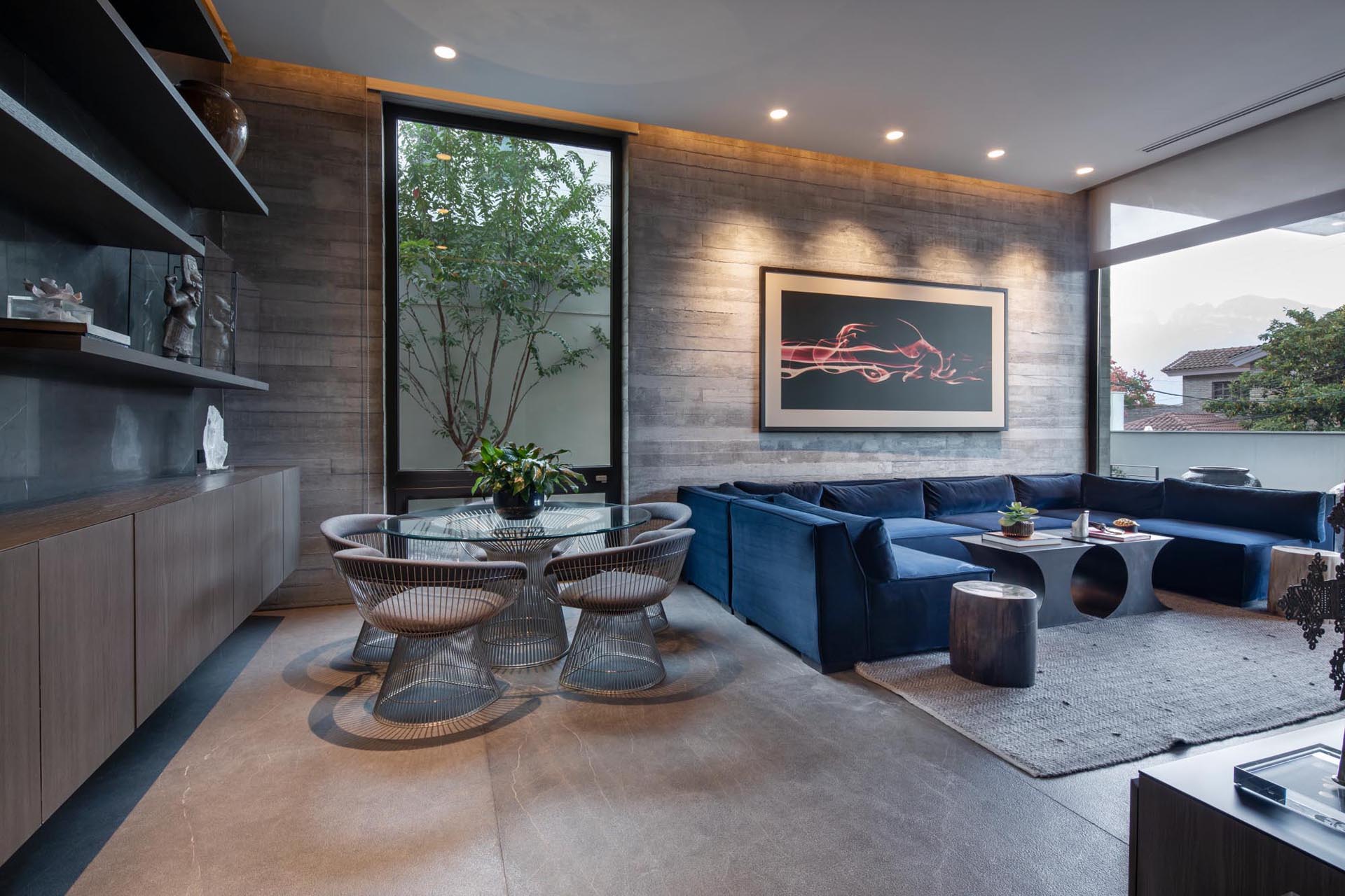 A modern living room with a u-shaped blue sofa, a dining area, and a board-formed concrete wall.