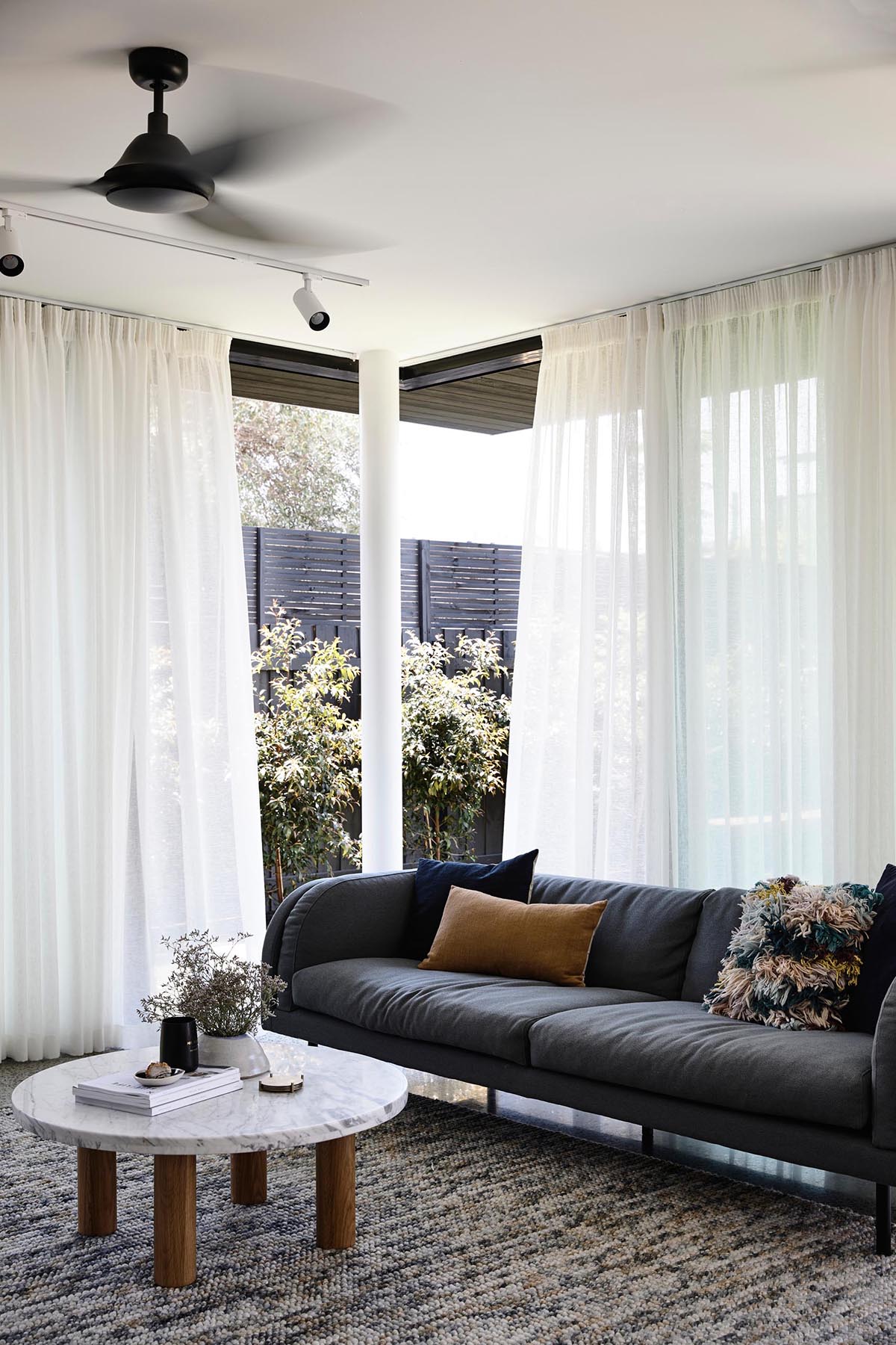 The glass walls of this modern home can be opened to connect the interior spaces, like the living room, to the backyard. Floor to ceiling curtains allow the breeze to flow through, yet provide privacy at the same time.