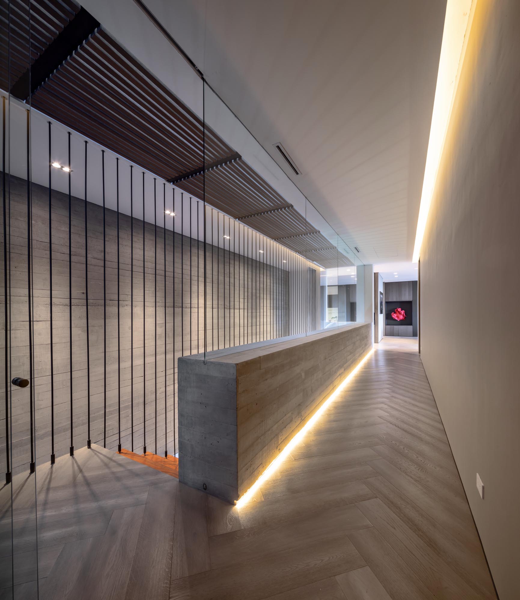 A modern hallway has a glass wall and hidden lighting incorporated into the floor and ceiling levels.