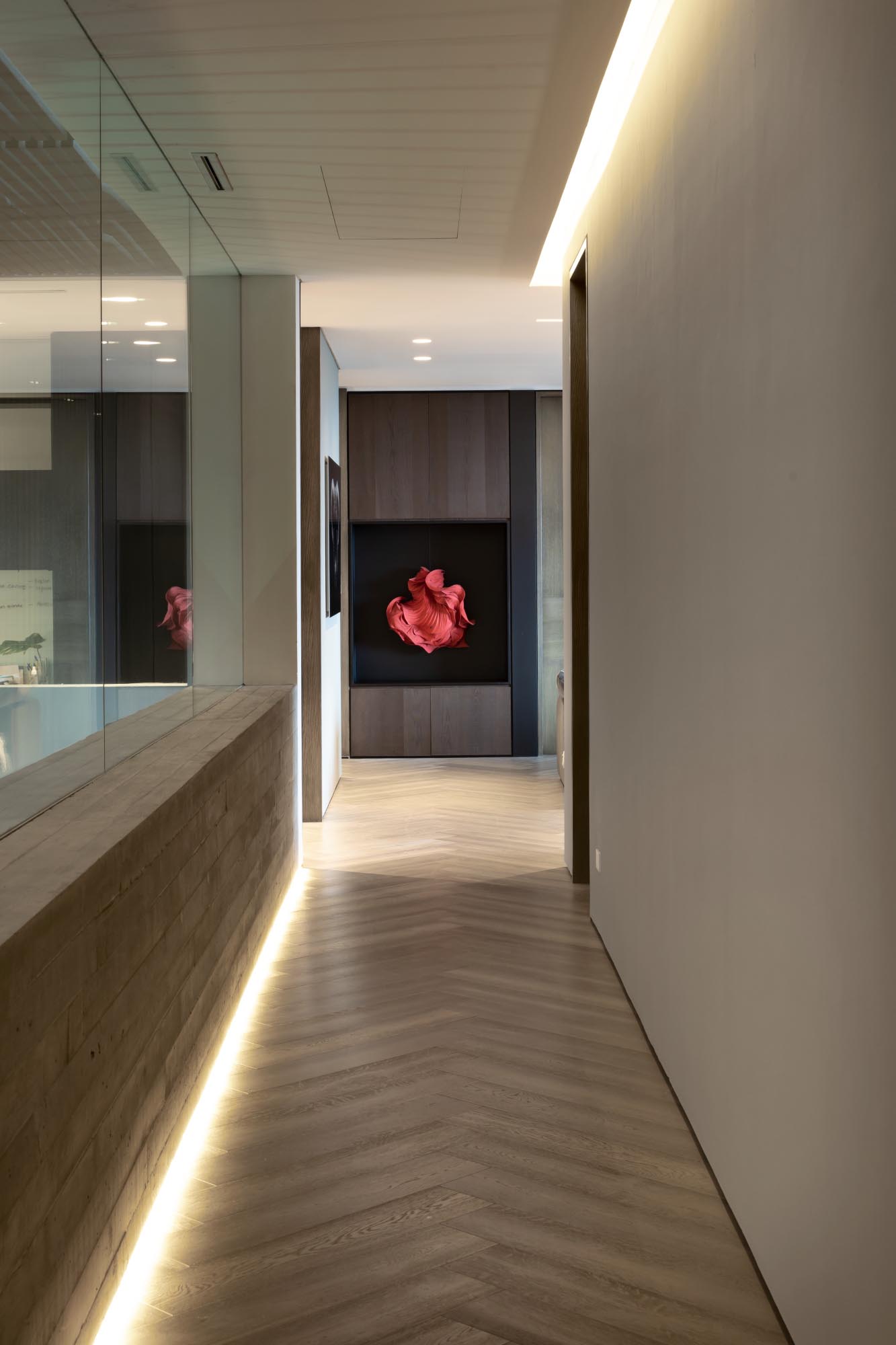 A modern hallway has a glass wall and hidden lighting incorporated into the floor and ceiling levels.