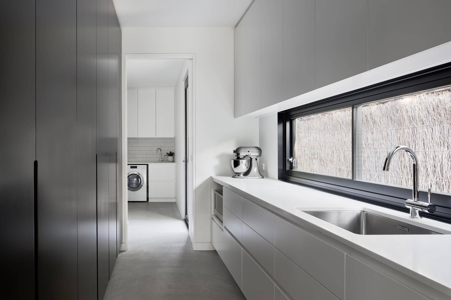 A modern pantry with black floor-to-ceiling cabinets on one wall, and white cabinetry on the other. Plus there's access to the laundry.