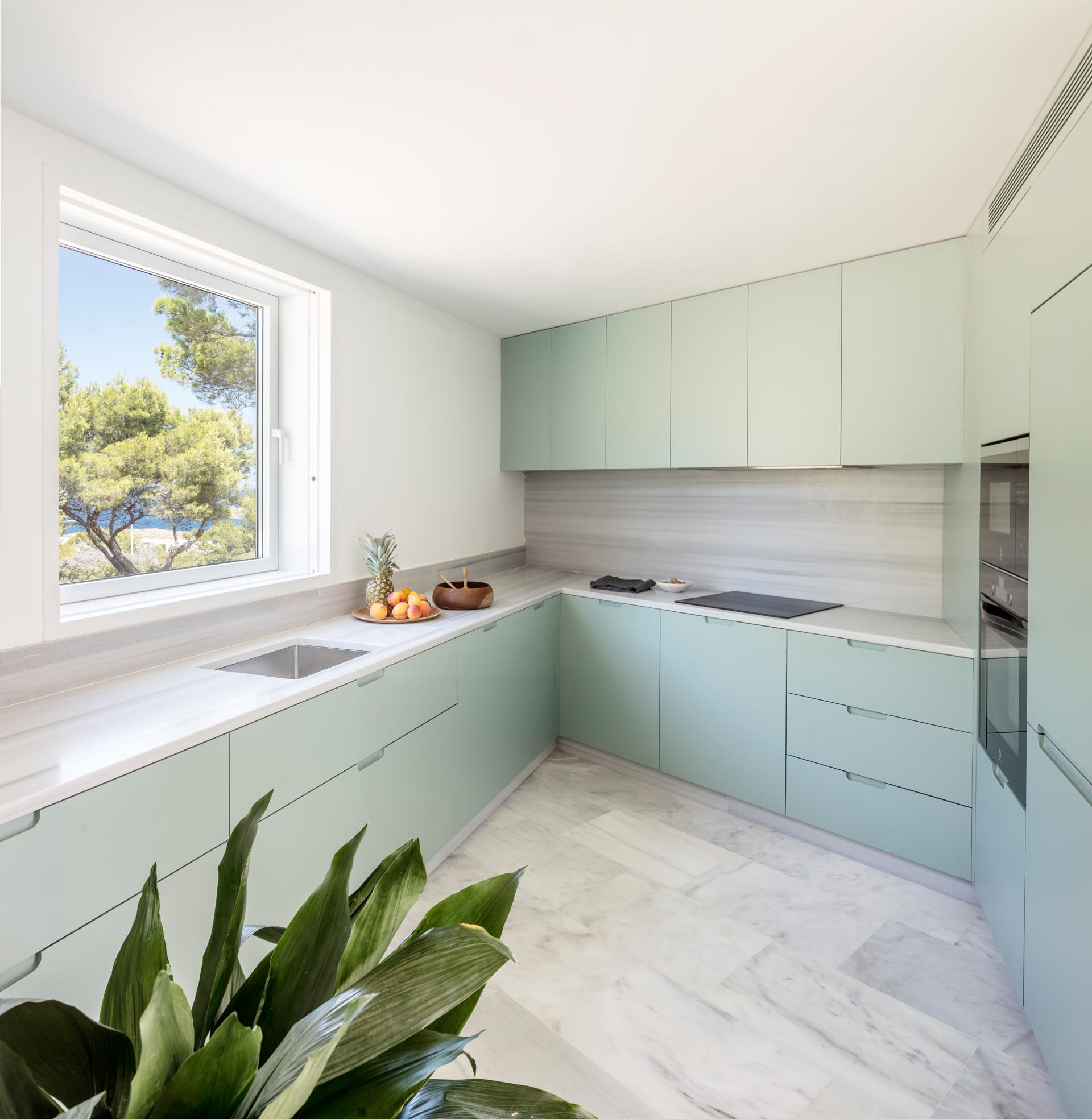 A modern kitchen with pastel green cabinets and a marble countertop and backsplash.