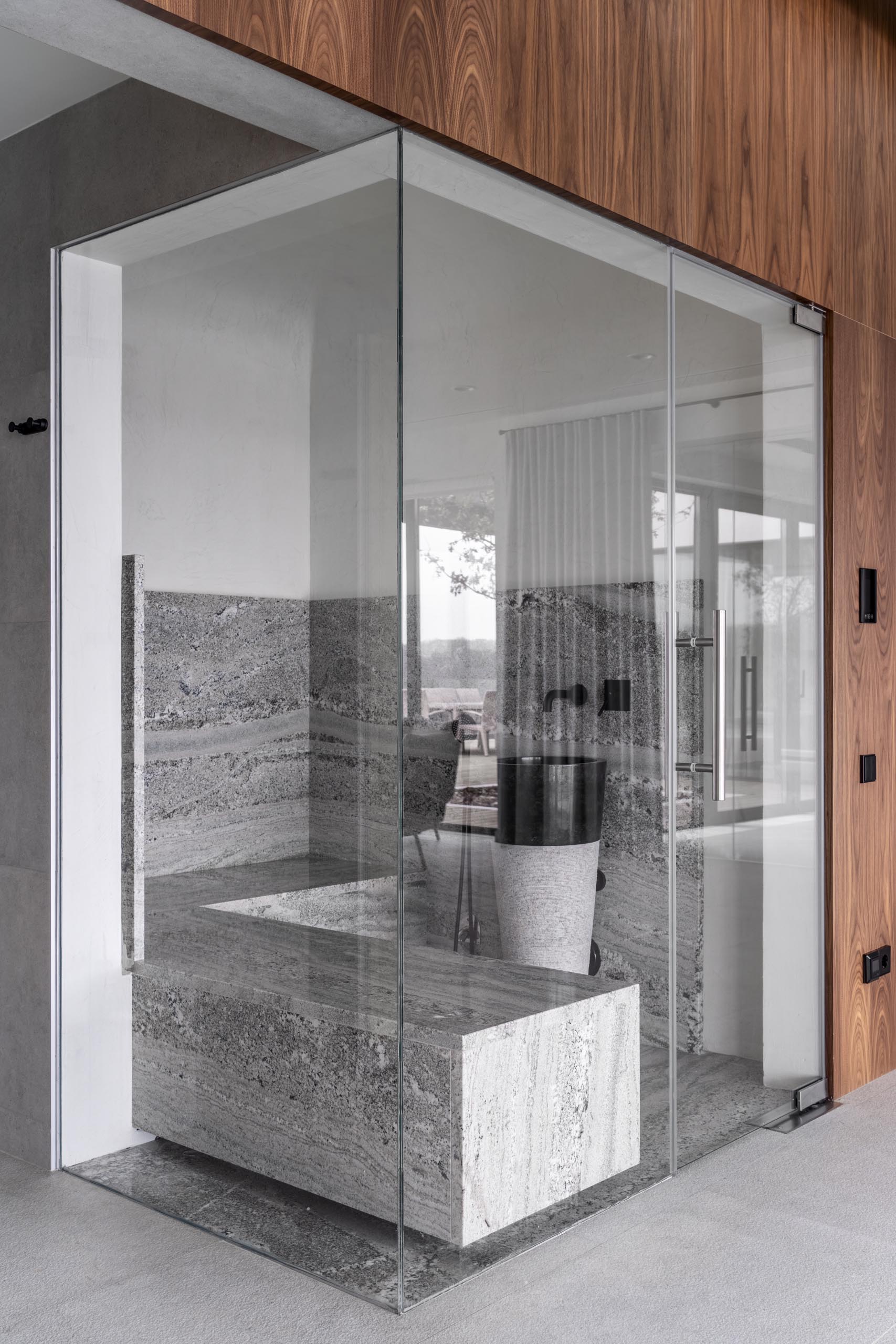 A sauna with glass walls, gray stone, and black accents.