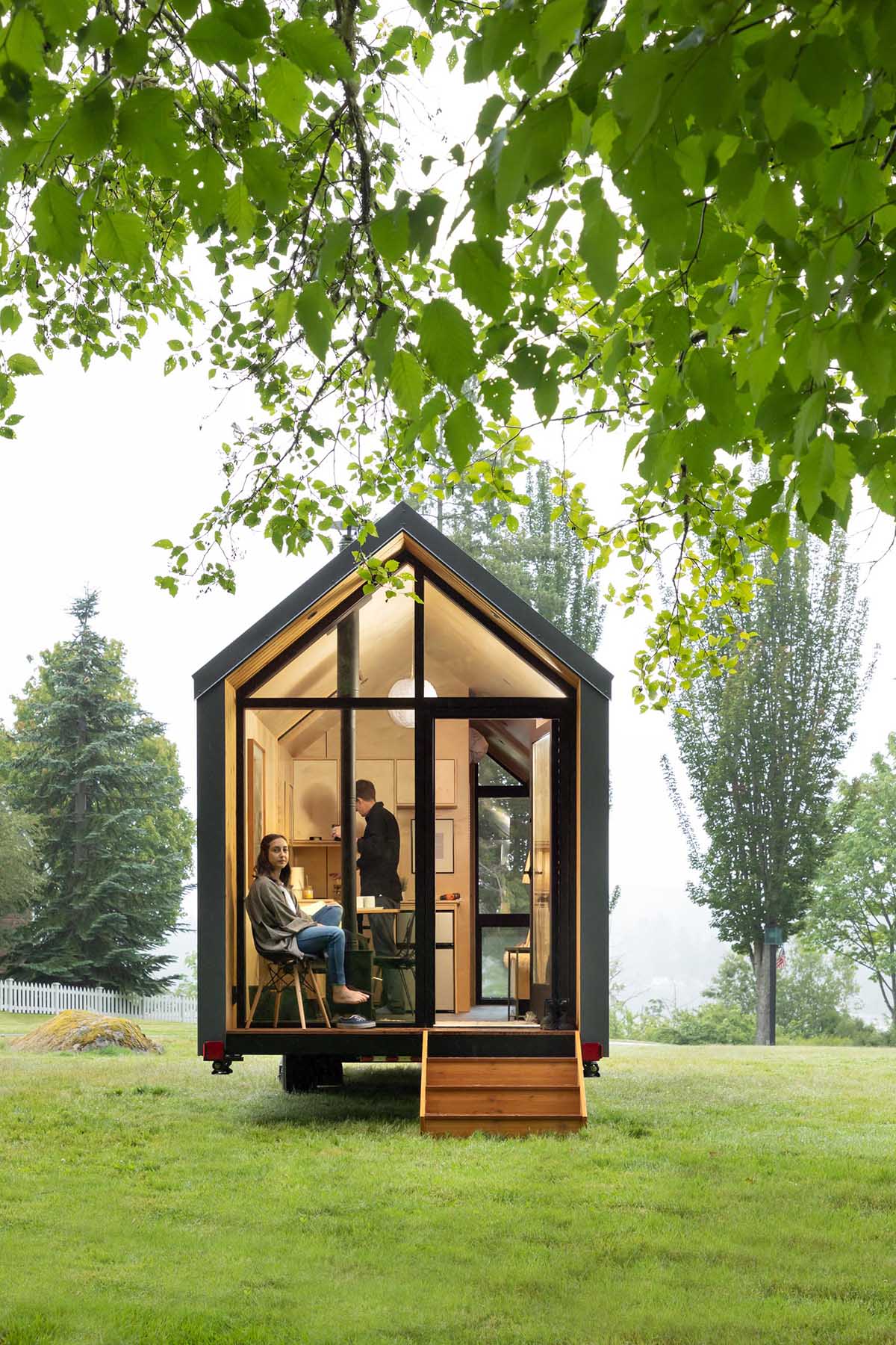 A wall of windows with a door at one end of this modern tiny home allows for natural light to filter through, and creates a connection to the small porch and the outdoors.