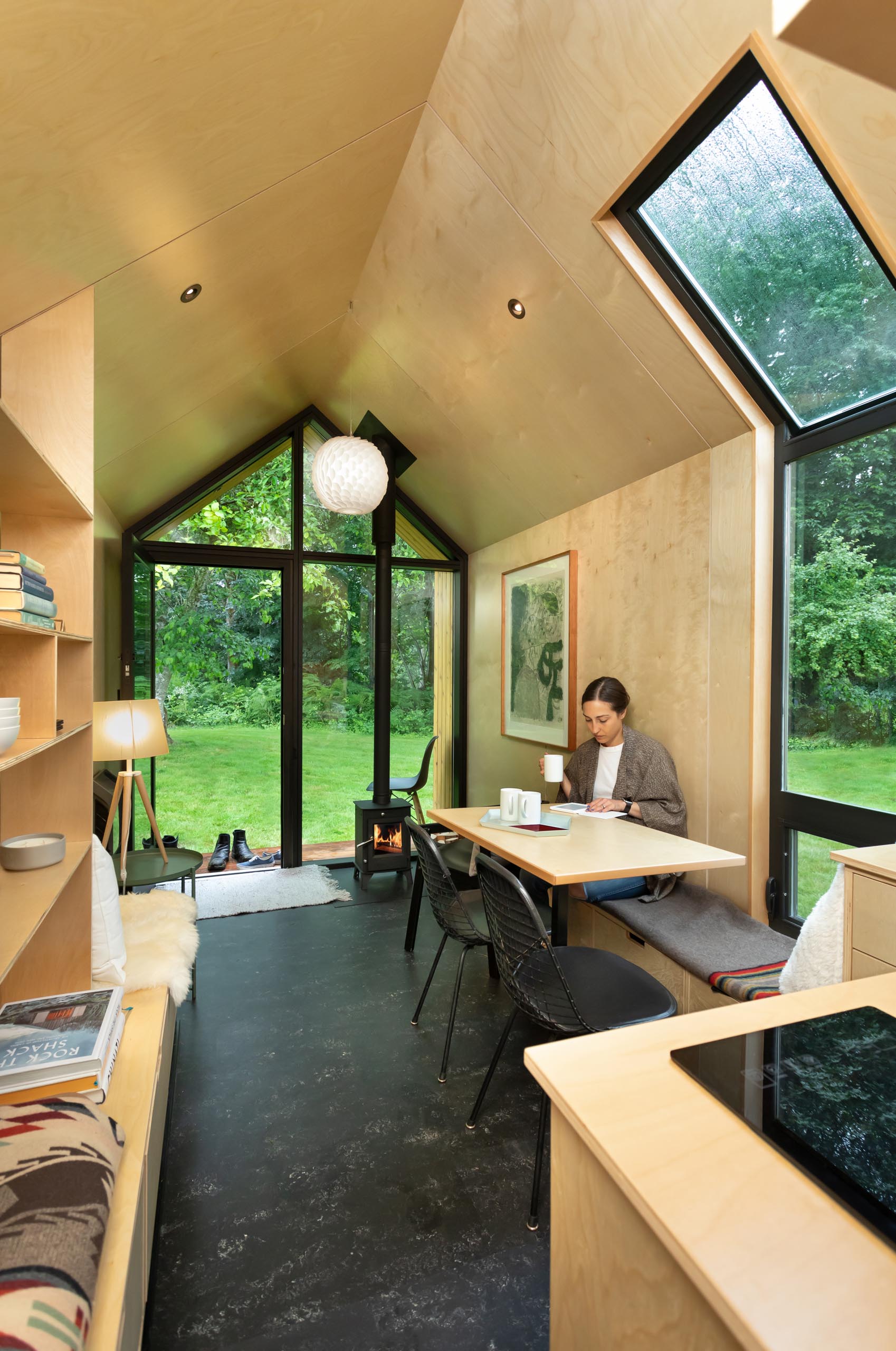 A modern tiny home with built-in benches, a wood burning stove, matte black linoleum flooring, and a small porch.