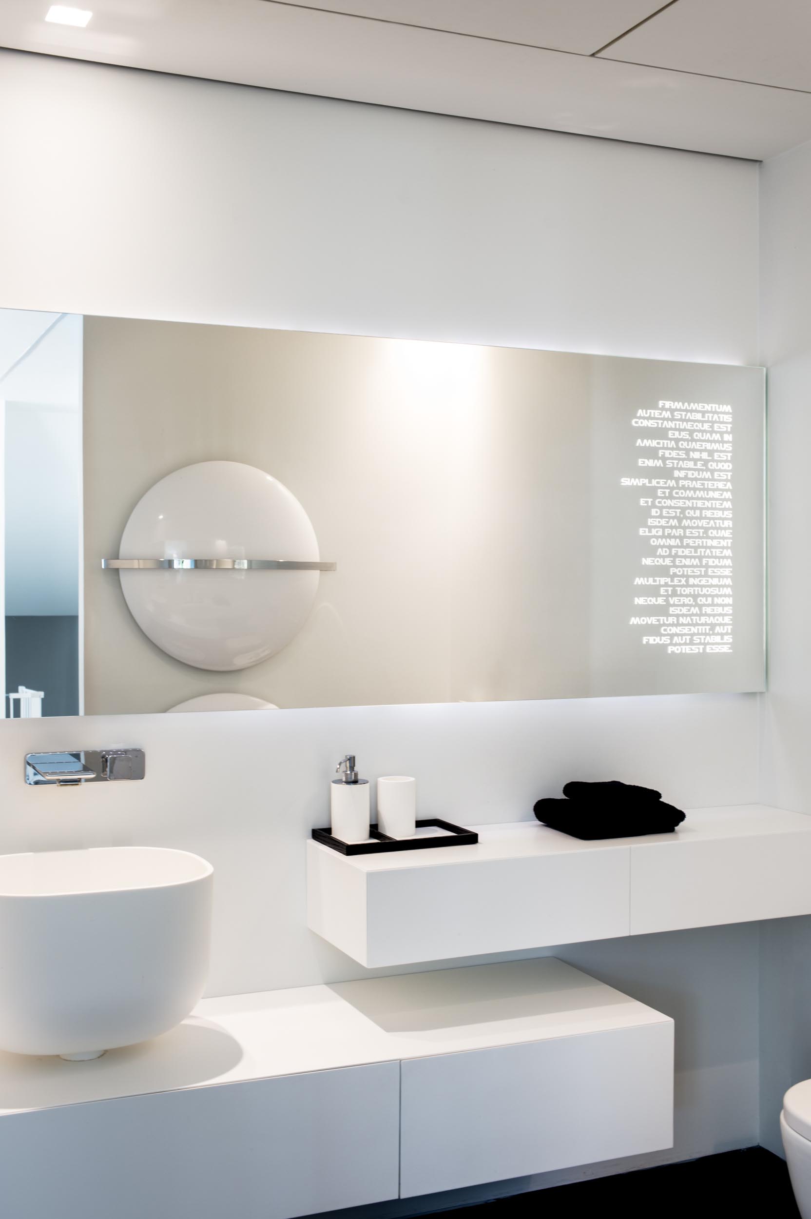 A modern bathroom white a white vanity and backlit mirror.