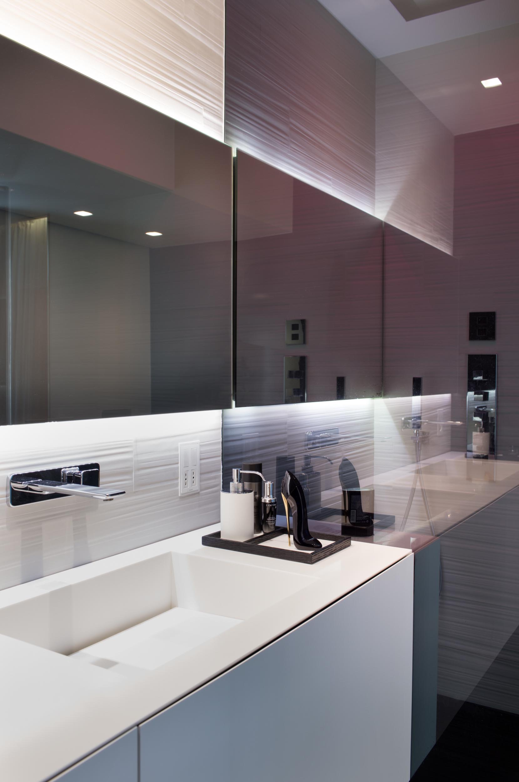 A modern bathroom with a white vanity and backlit mirror.