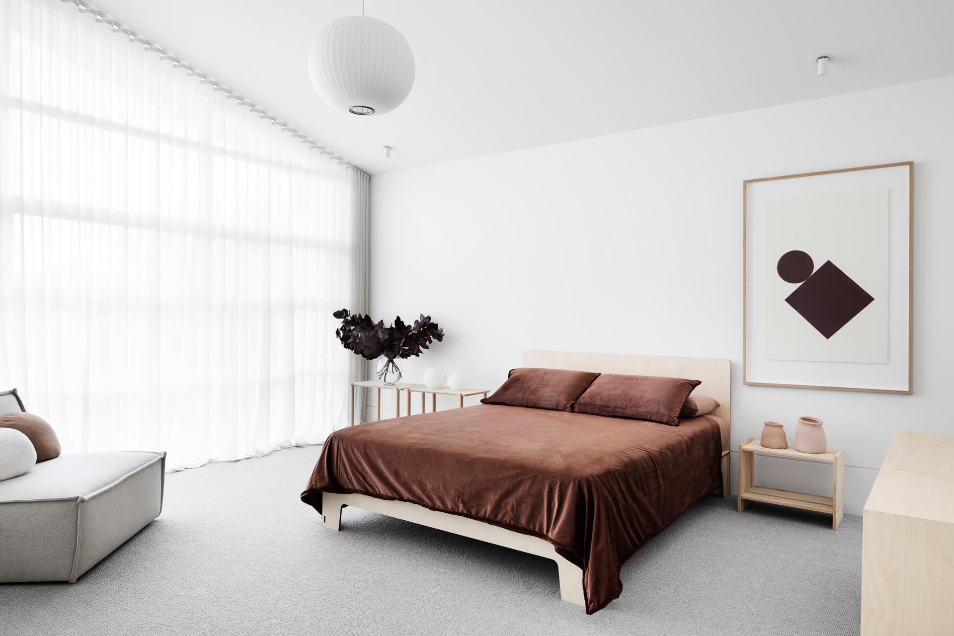 Trong phòng ngủ chính này, bộ đồ giường màu nâu sẫm tương phản với các yếu tố sáng hơn trong phòng, như sàn, bàn cạnh giường và ghế bọc.  